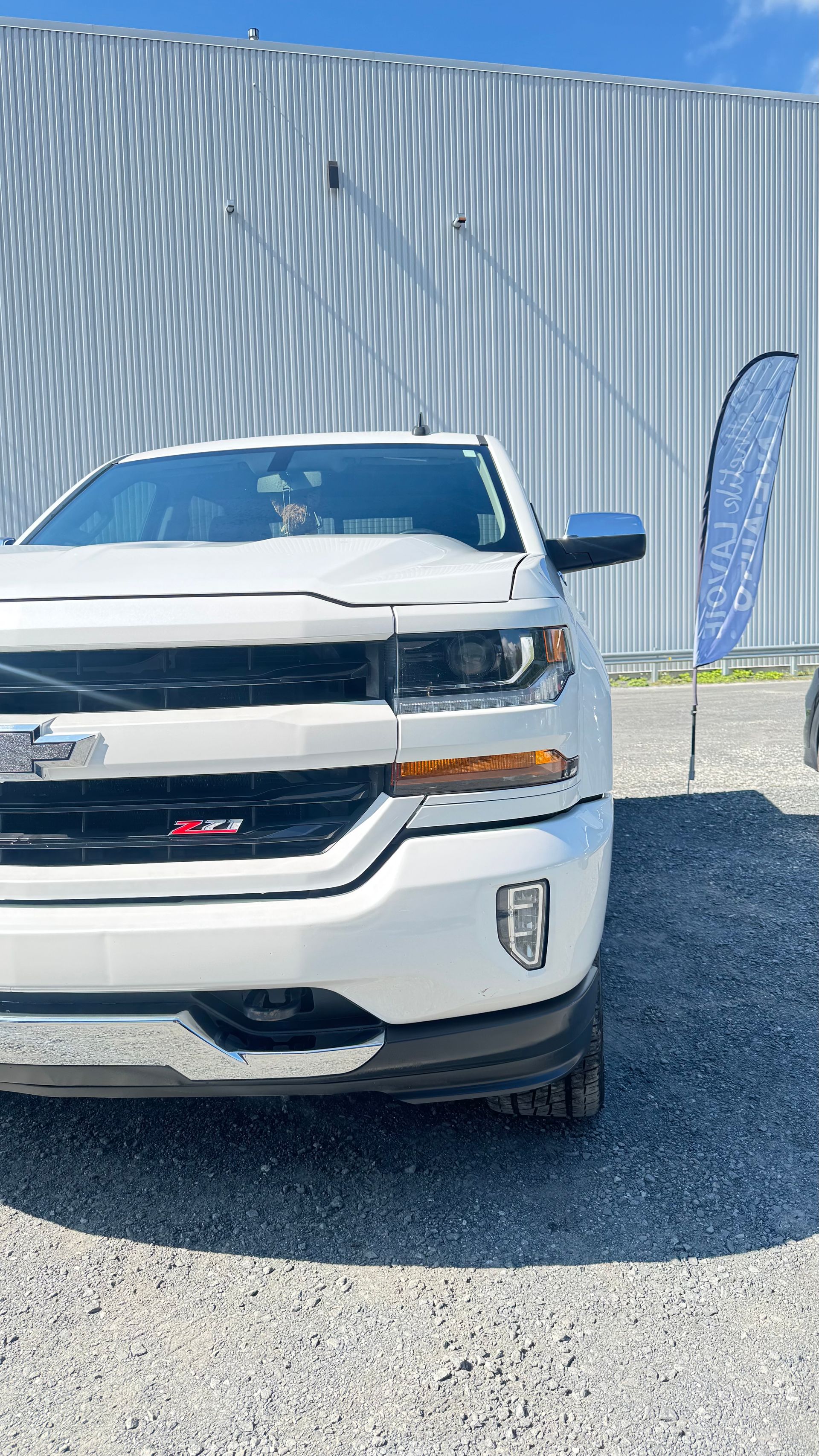 Camionnette Chevrolet blanche garée devant un bâtiment en tôle ondulée par une journée ensoleillée.