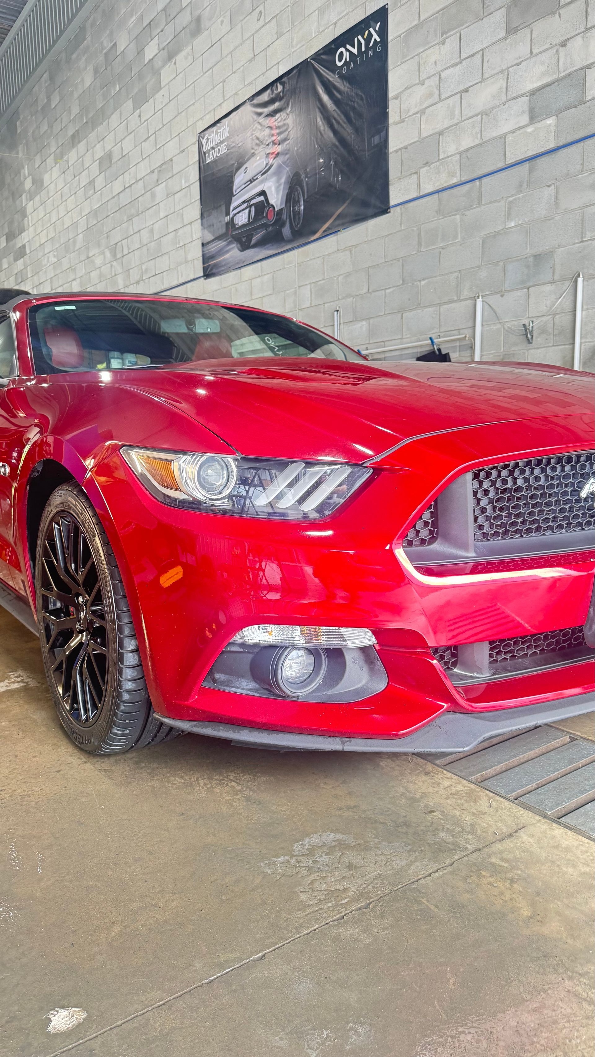 Ford Mustang rouge dans une station de lavage avec des roues noires.