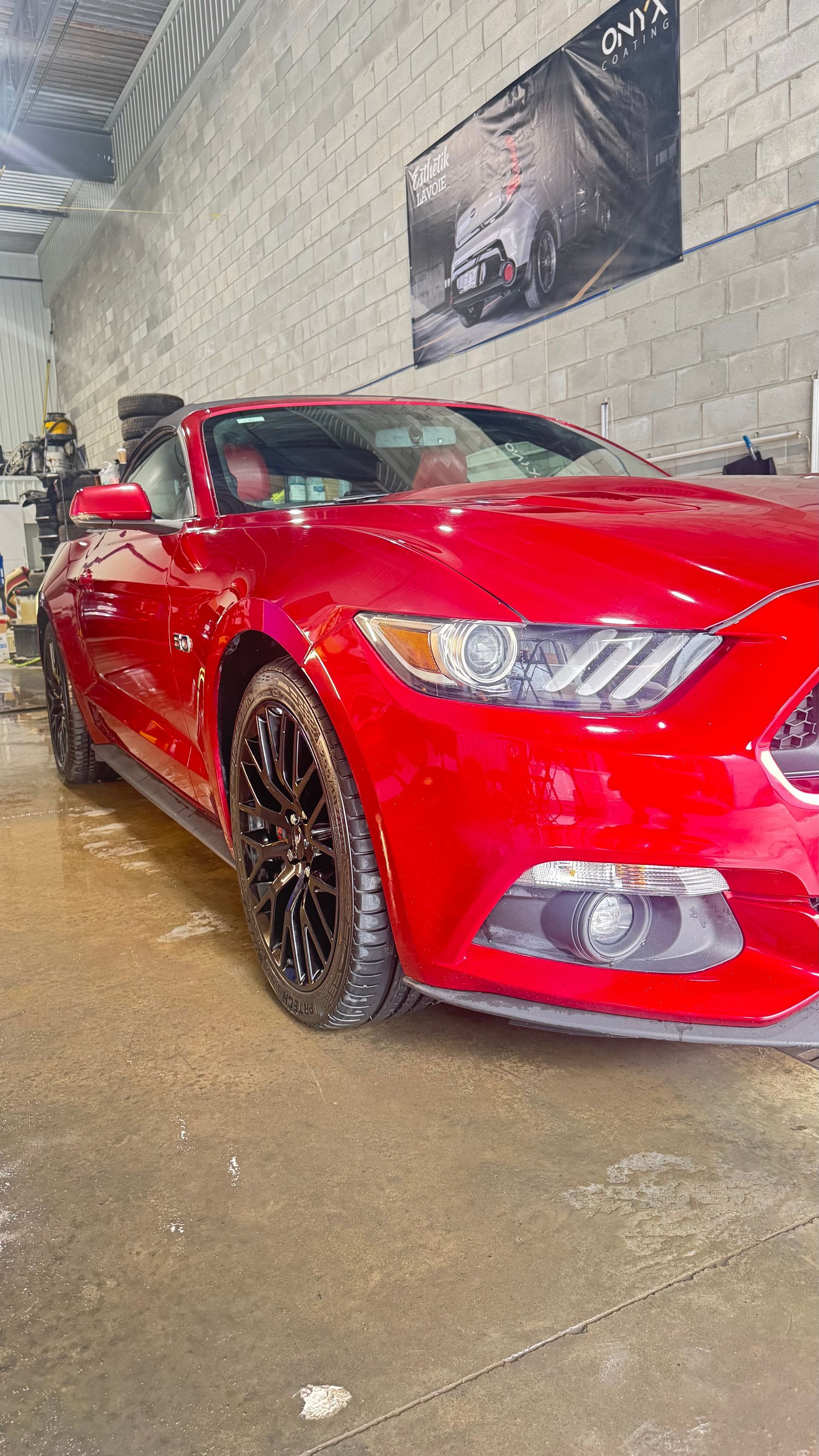 Ford Mustang rouge lavée dans un lave-auto, avec des roues noires, dans un garage.