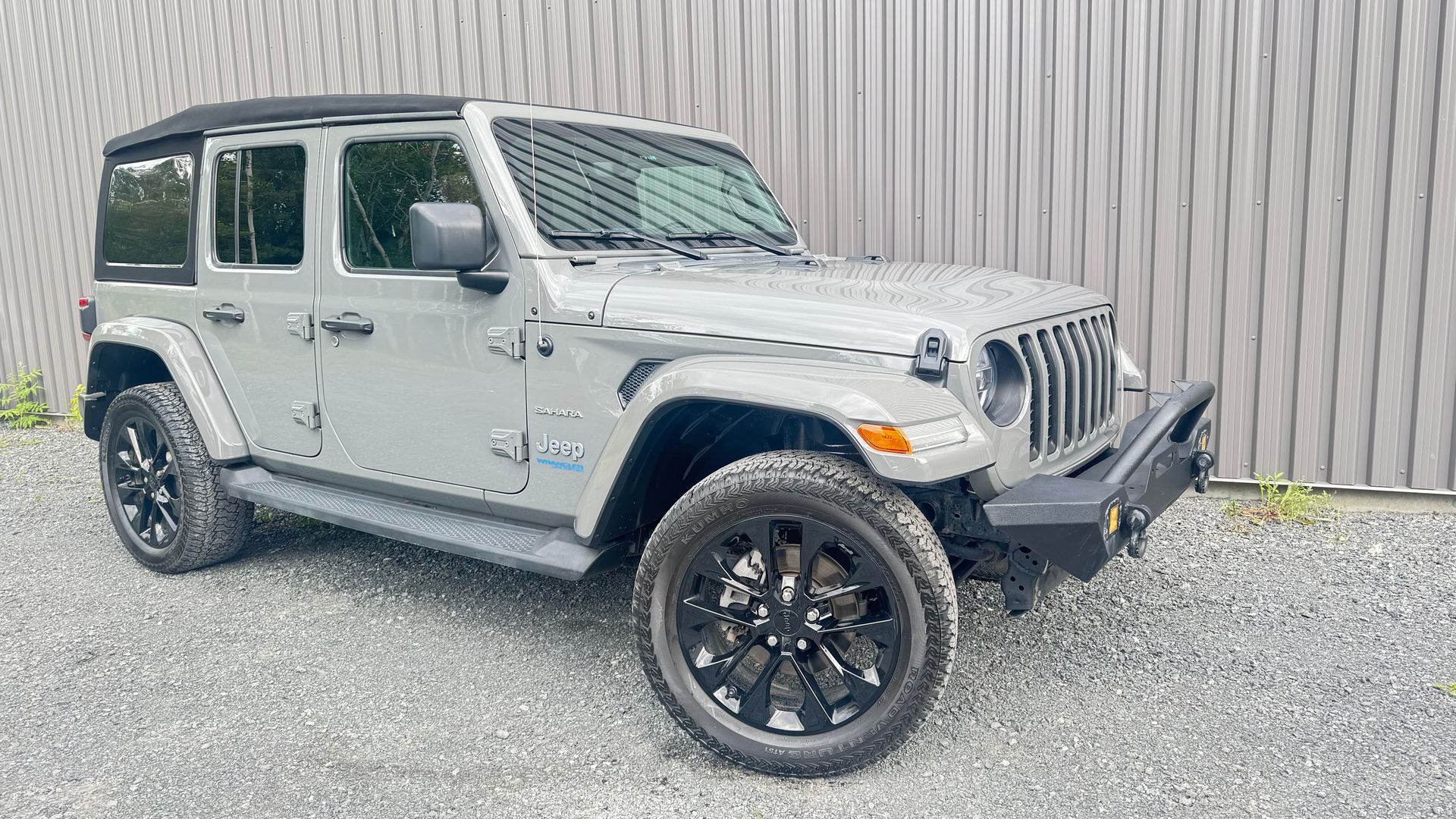 Jeep Wrangler grise garée à l'extérieur avec des roues noires et un pare-chocs avant noir.