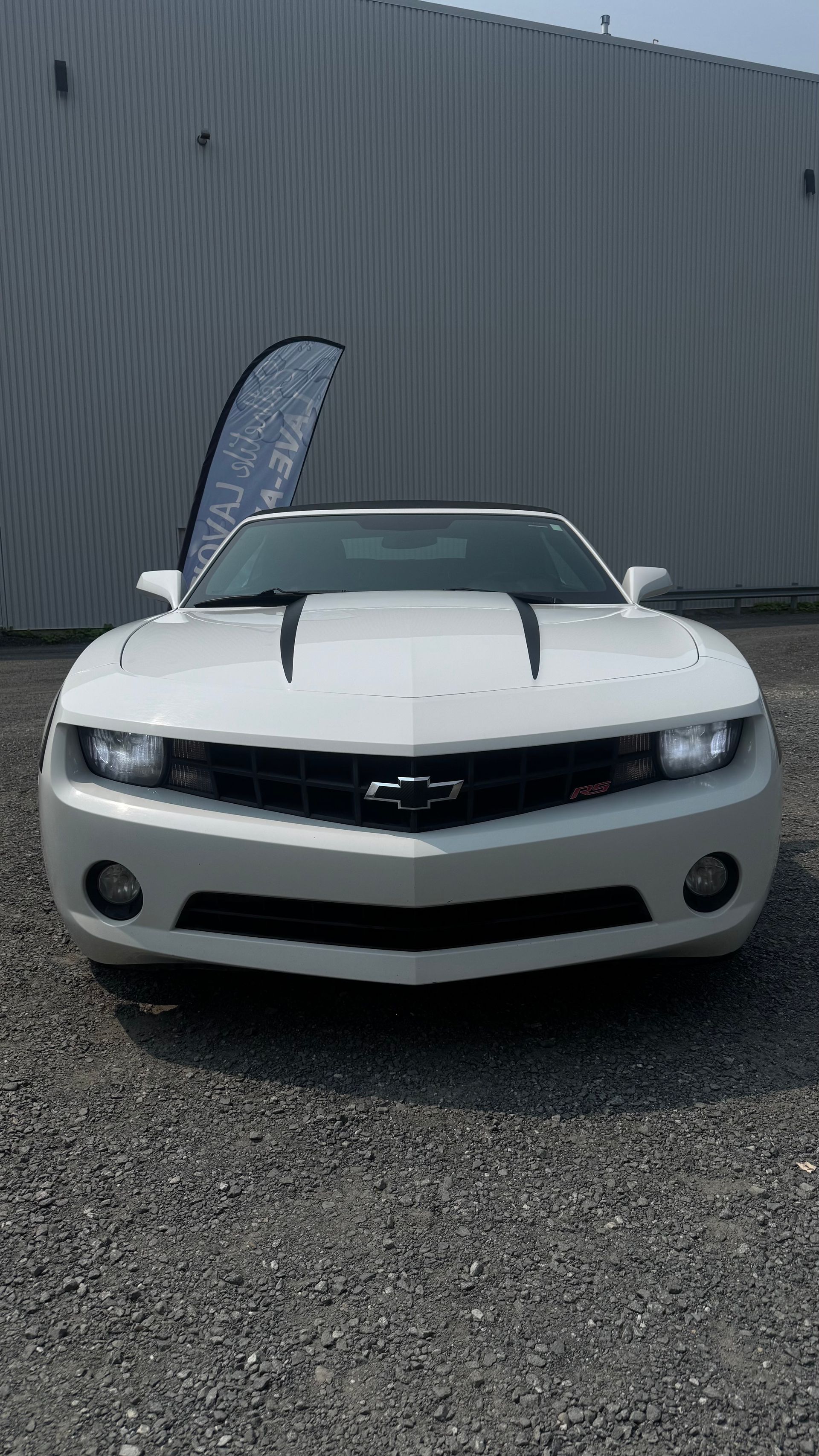 Chevrolet Camaro blanche garée devant un bâtiment avec une banderole.