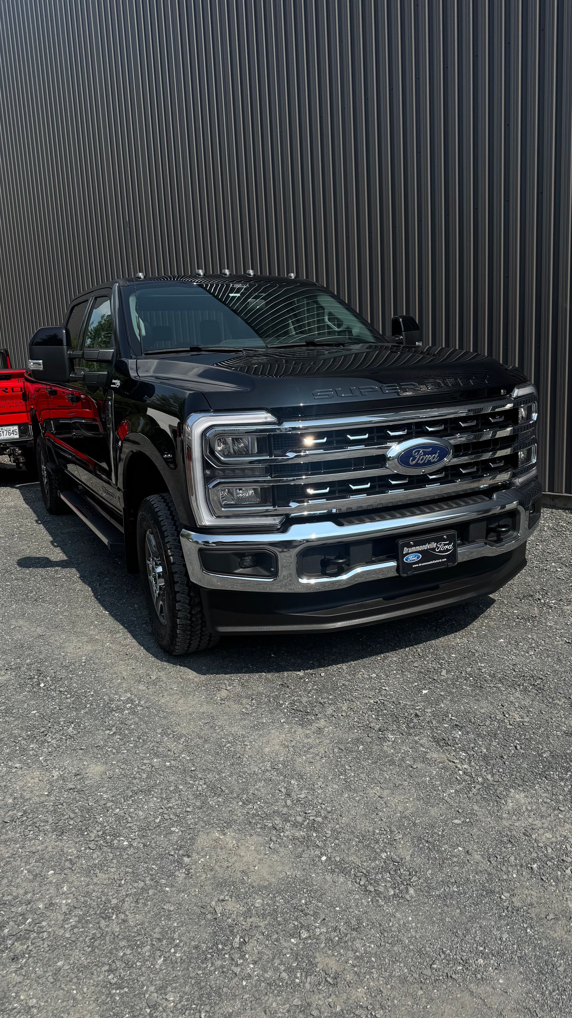 Camionnette Ford noire garée sur du gravier devant un mur en tôle ondulée.