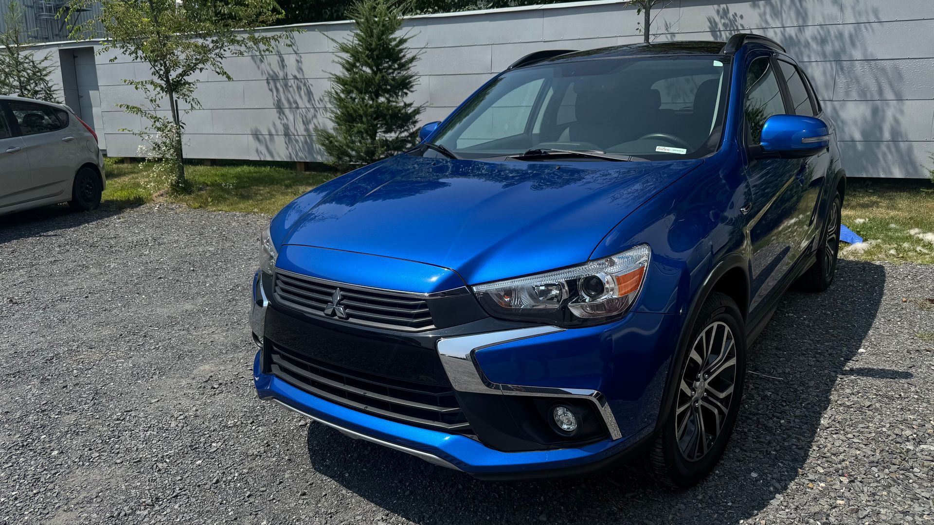 SUV Mitsubishi bleu garé sur du gravier, journée ensoleillée.
