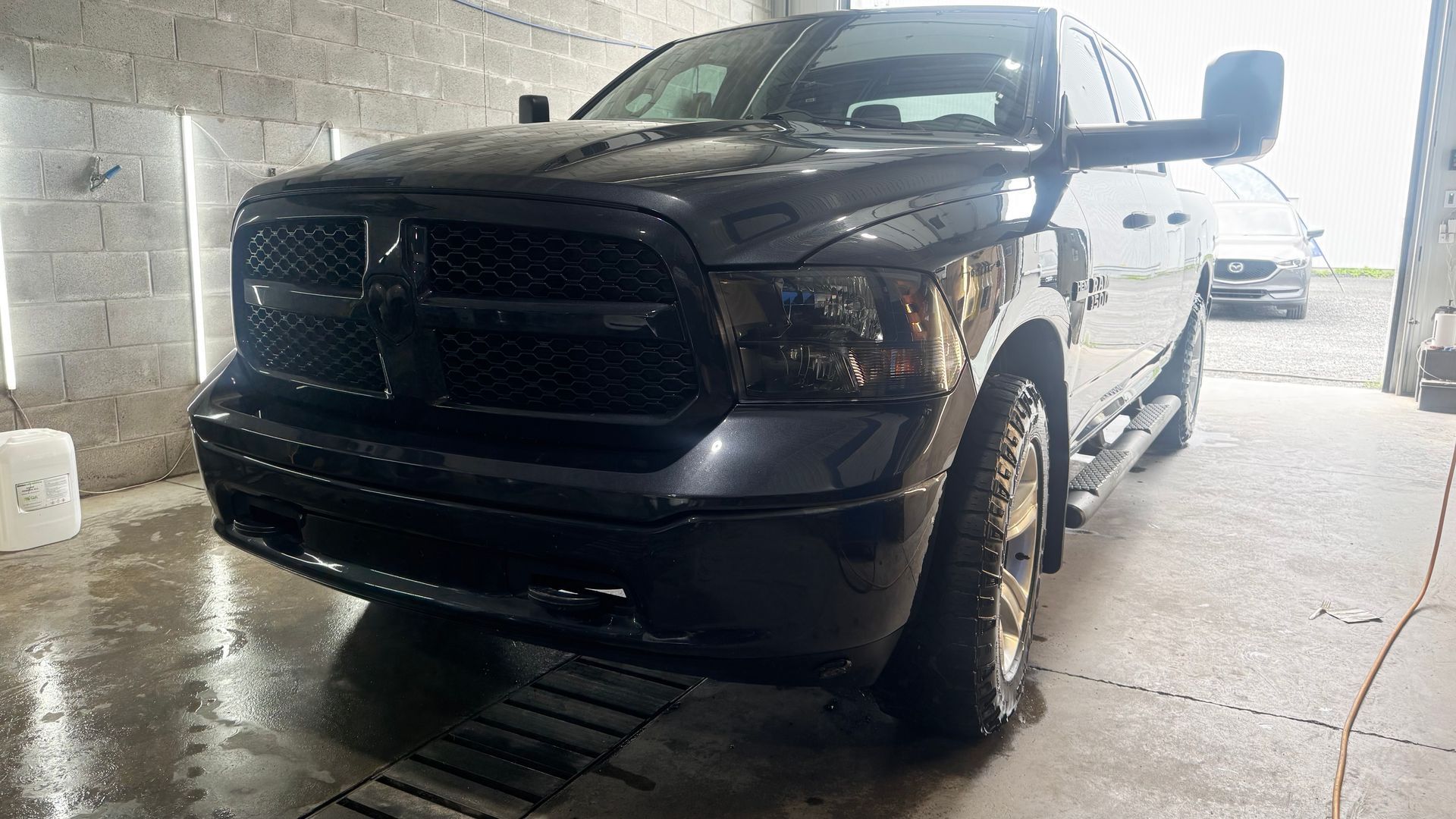 Camionnette Dodge Ram noire garée dans une baie de lavage de voiture, vue de face, chaussée mouillée.
