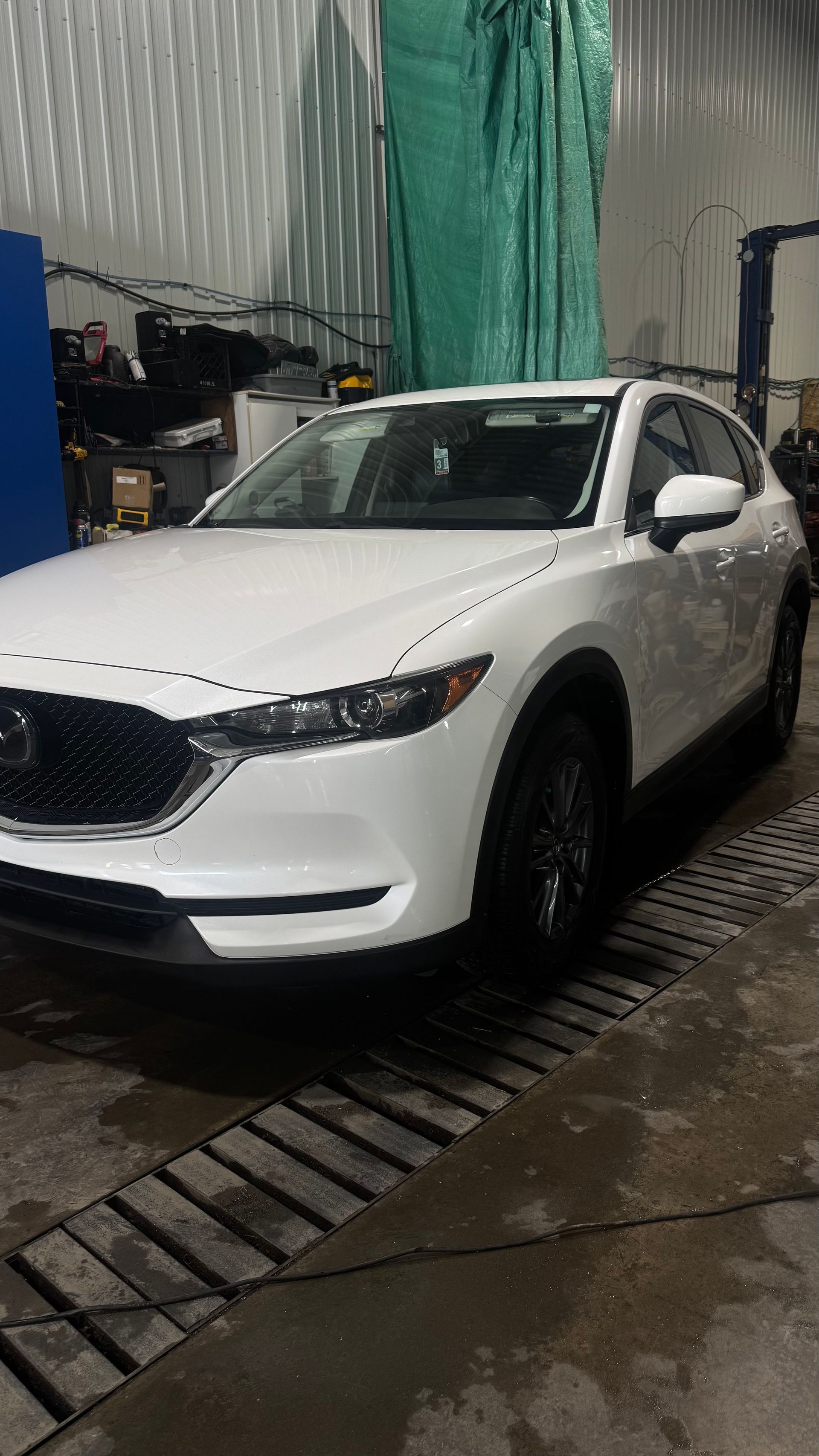 SUV Mazda blanc dans un atelier automobile, sol mouillé.