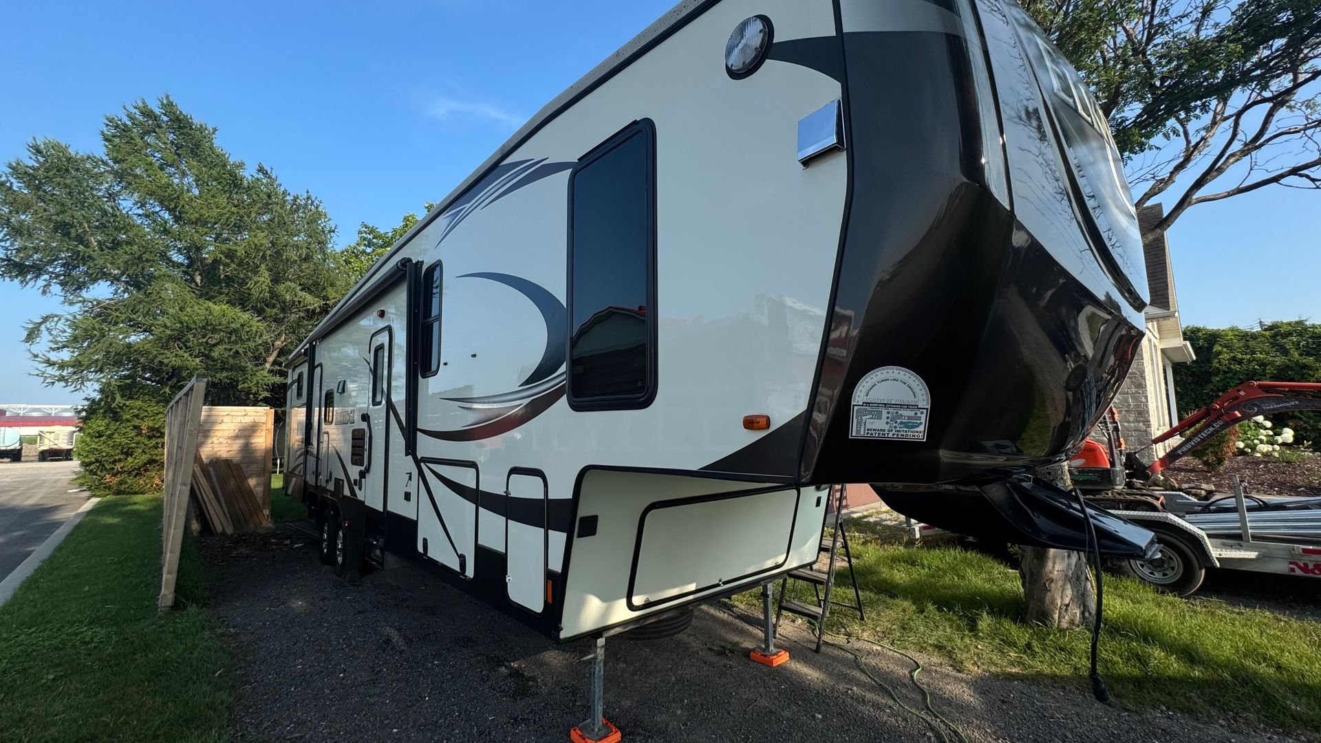 Un grand camping-car à sellette blanc et noir stationné sur l'herbe, avec des blocs de nivellement orange.