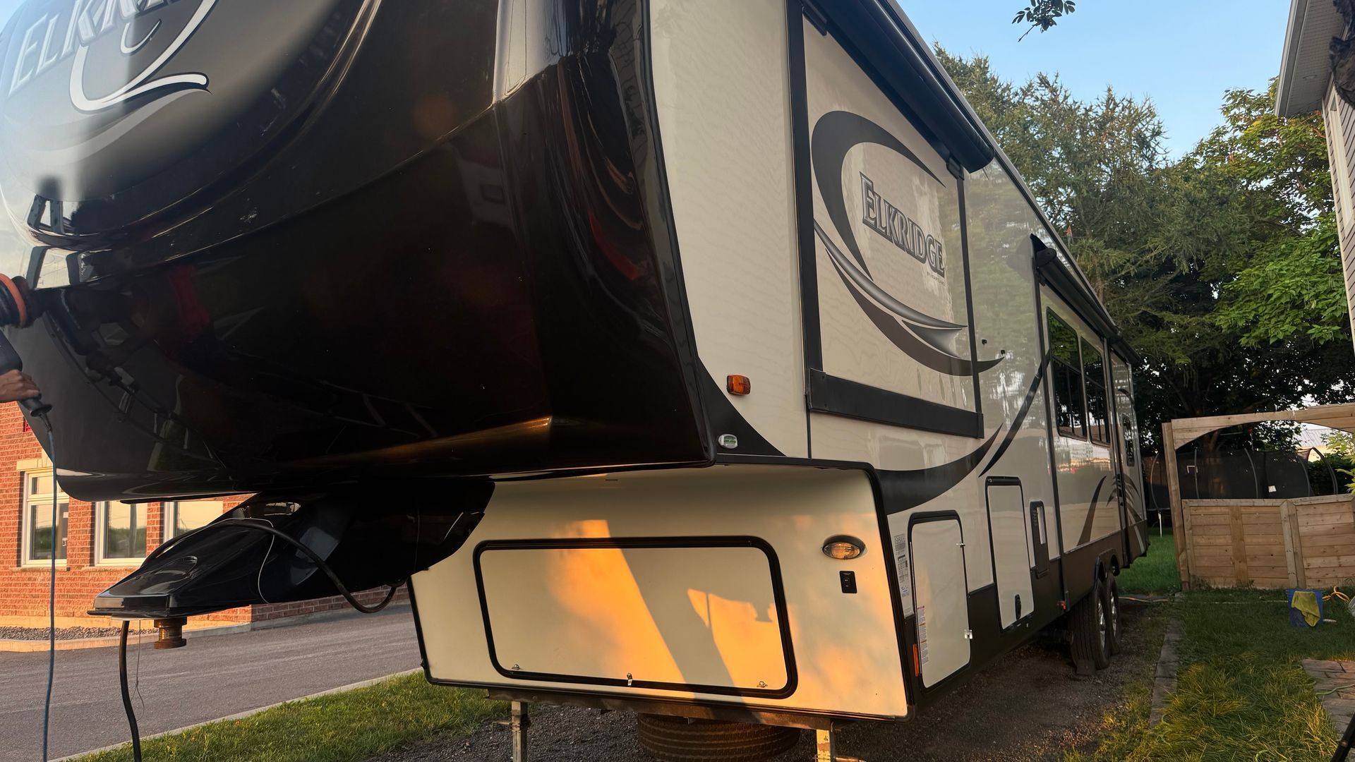 Camping-car garé devant un bâtiment. Couleurs beige et noir. L'auvent est déployé.