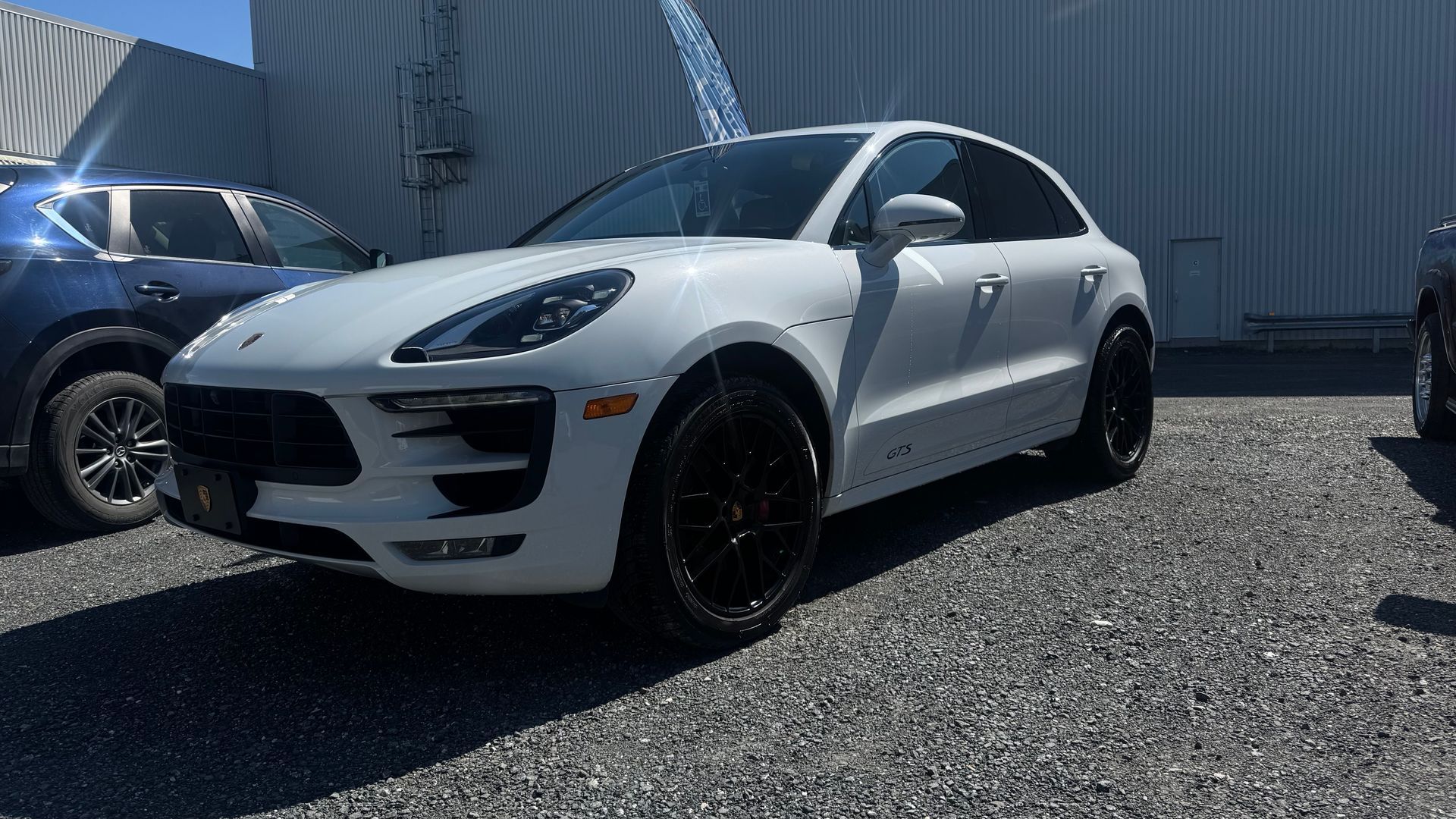 SUV Porsche Macan blanc avec roues noires garé sur du gravier.