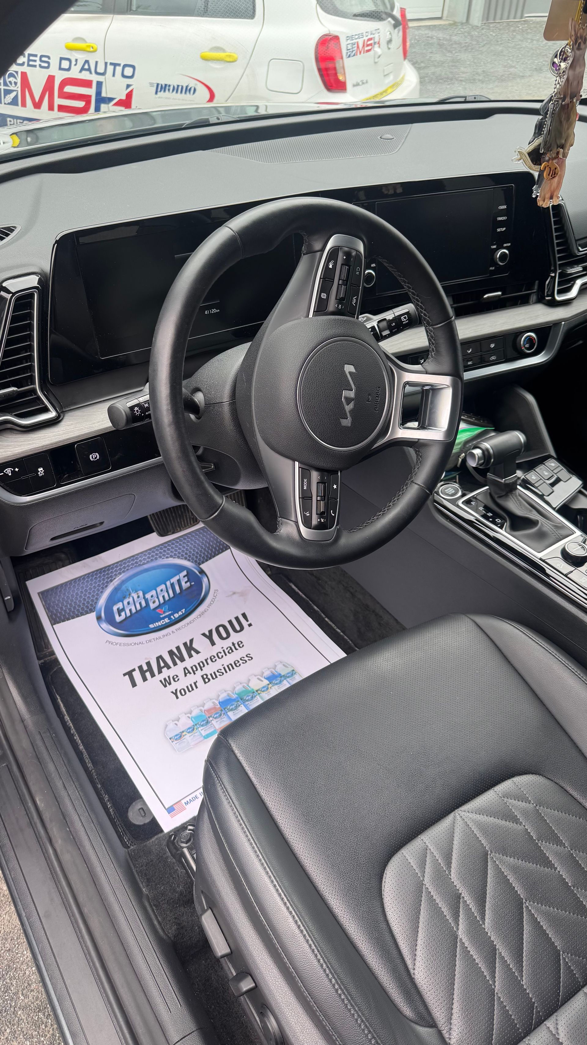 Vue intérieure d'une voiture Kia noire avec un siège en cuir et un tapis de sol « Merci ».