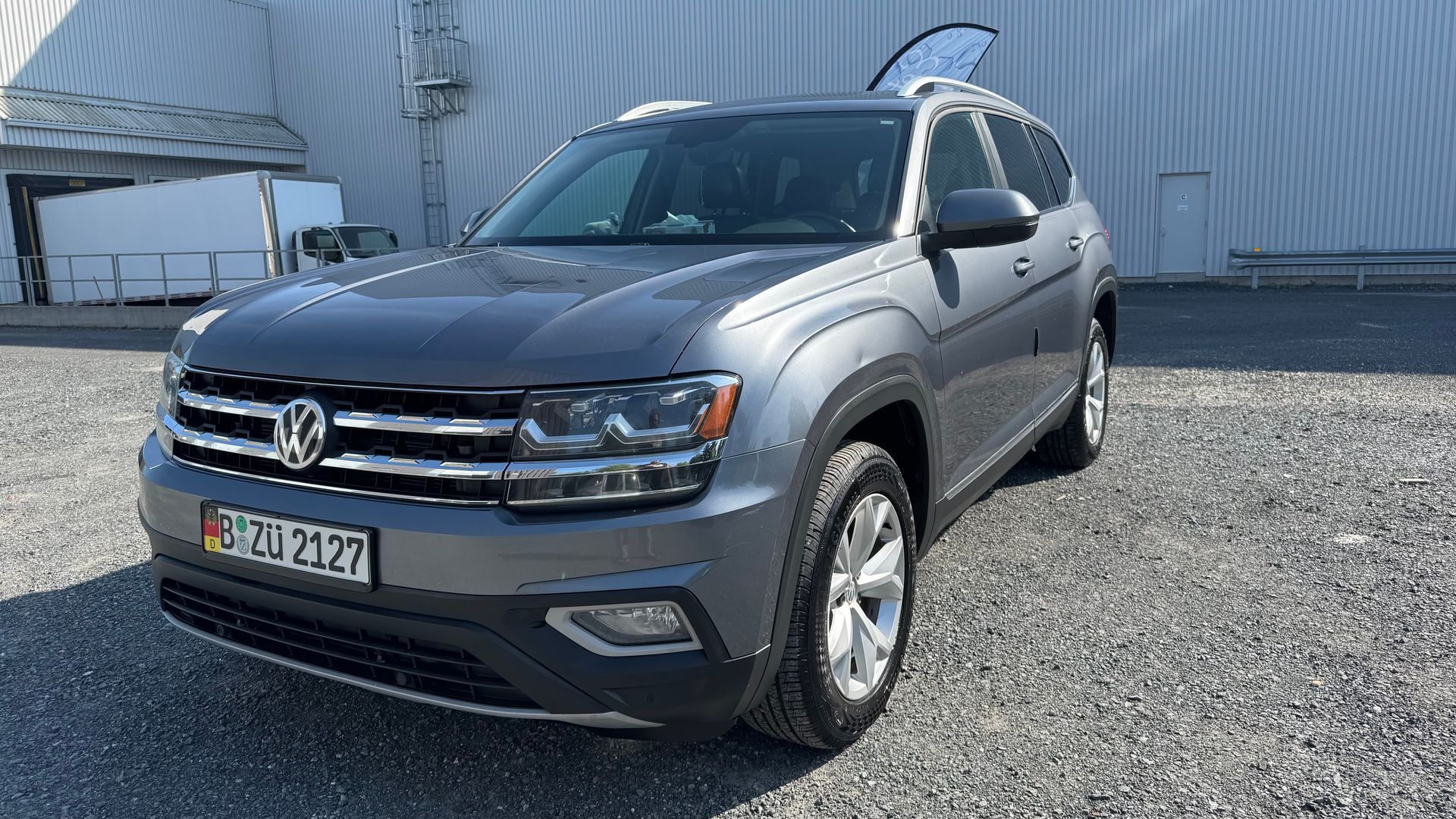 SUV Volkswagen Atlas gris avec une plaque d'immatriculation garé à l'extérieur près d'un bâtiment.