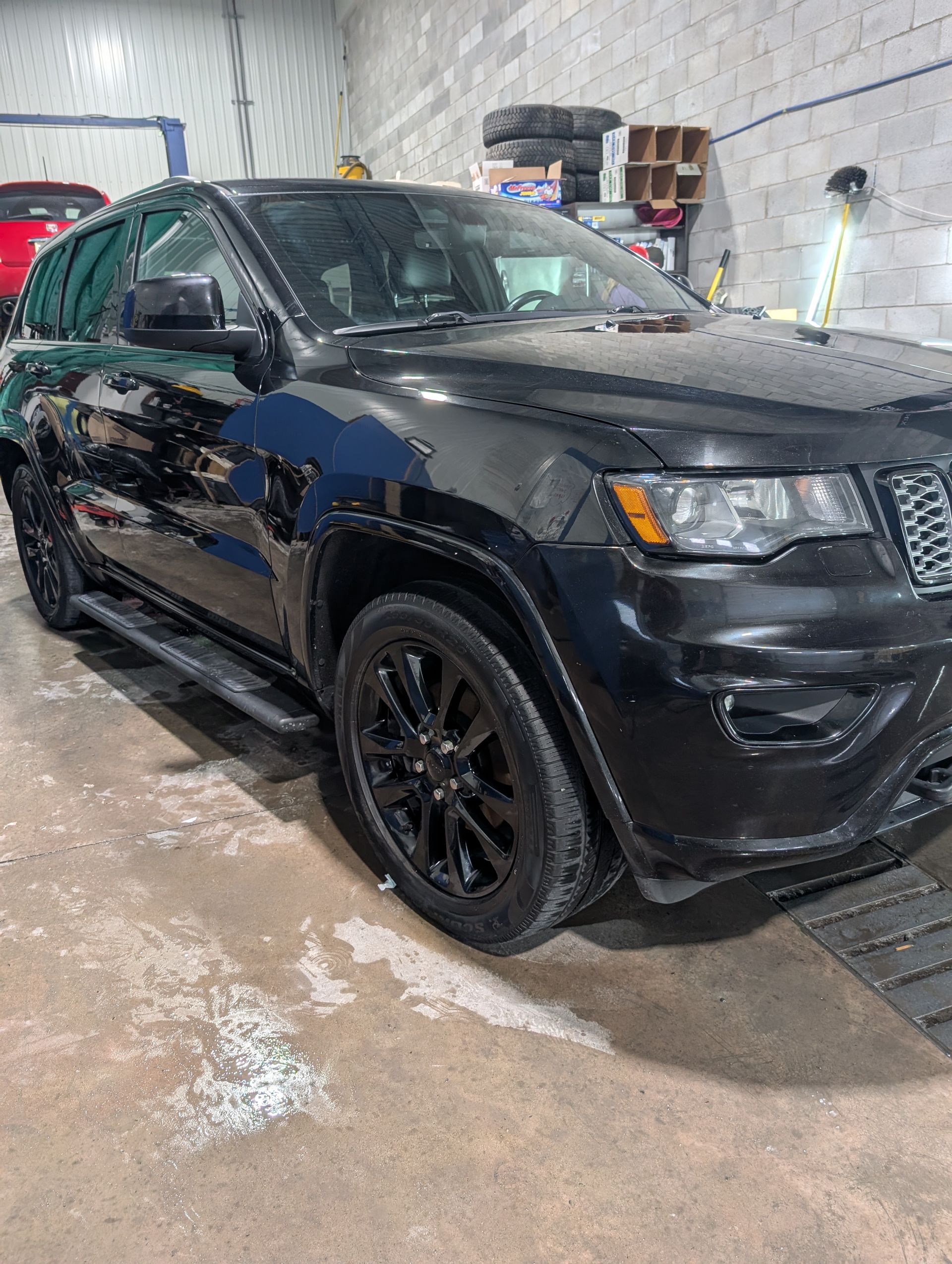 Jeep Grand Cherokee noir dans un garage avec roues noires et marchepieds latéraux.