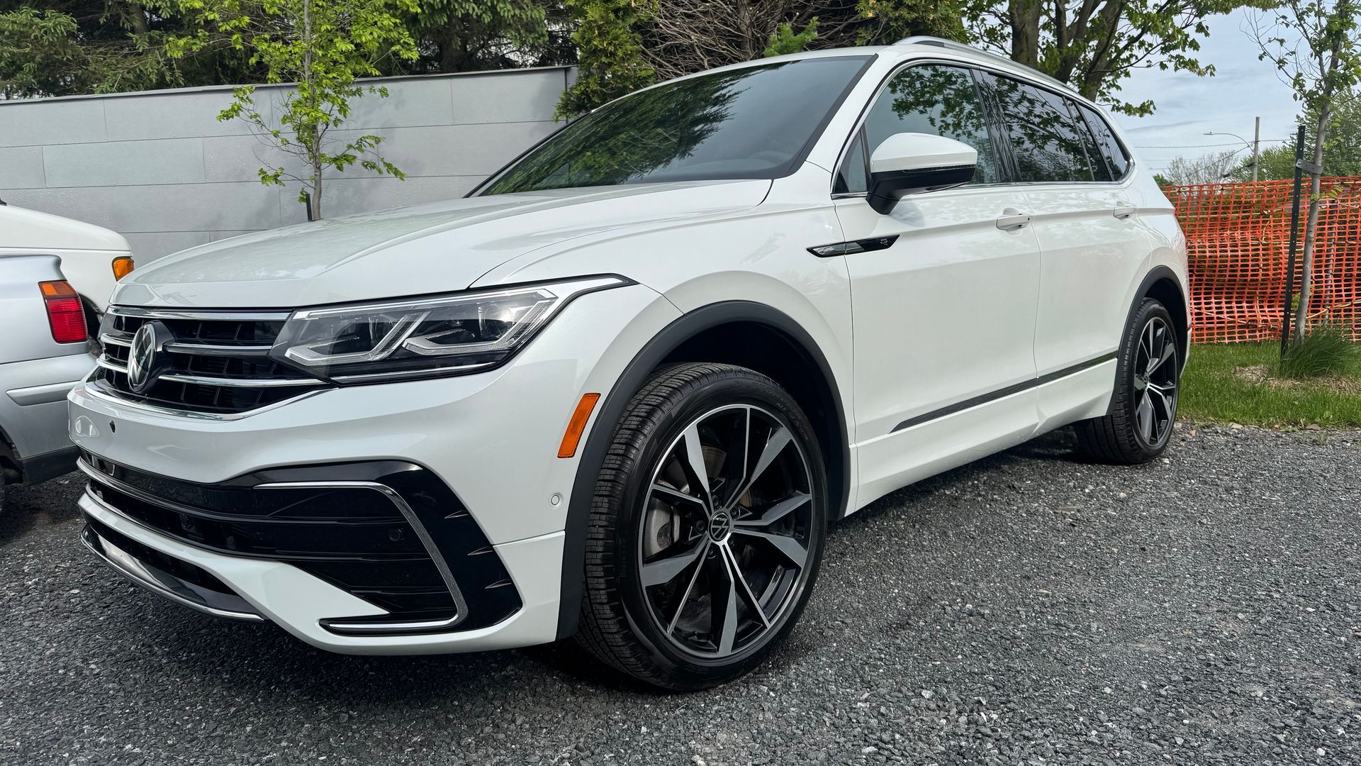 SUV Volkswagen Tiguan blanc garé sur du gravier, roues noires, journée ensoleillée.