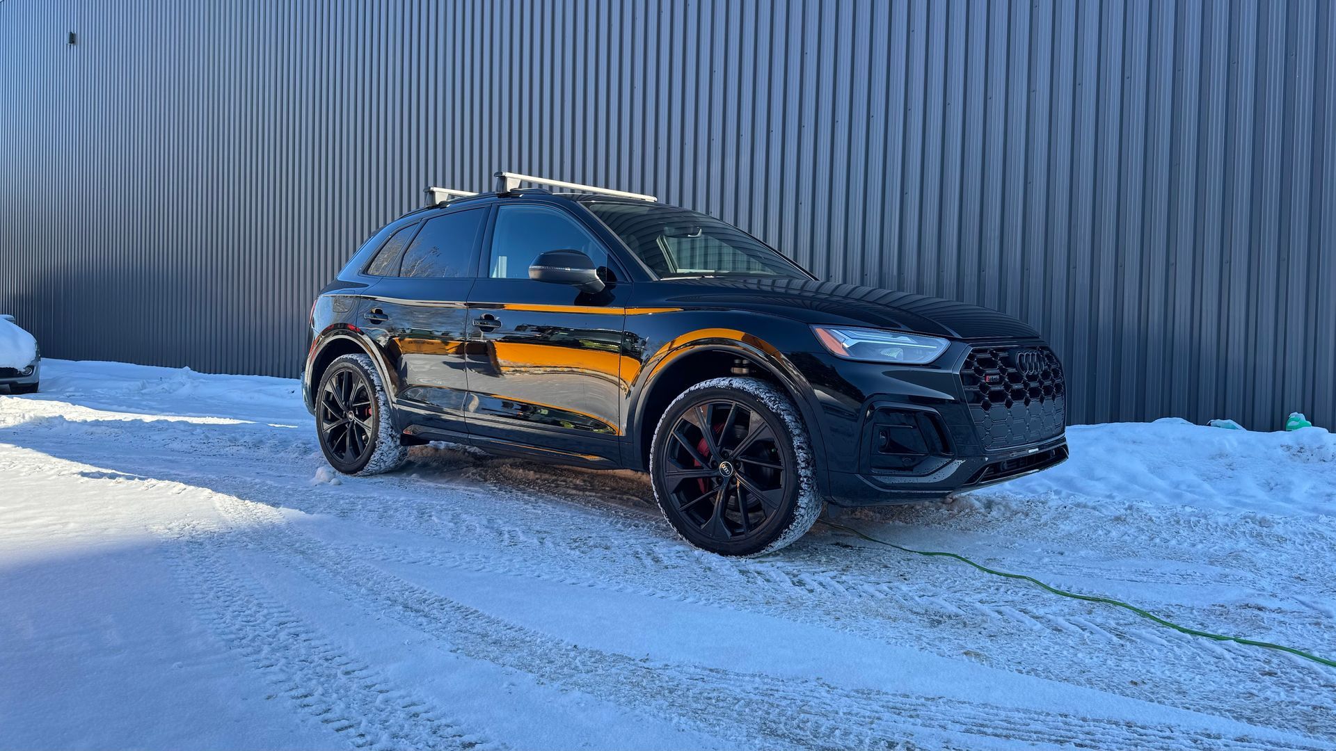 SUV noir garé sur la neige devant un mur gris.