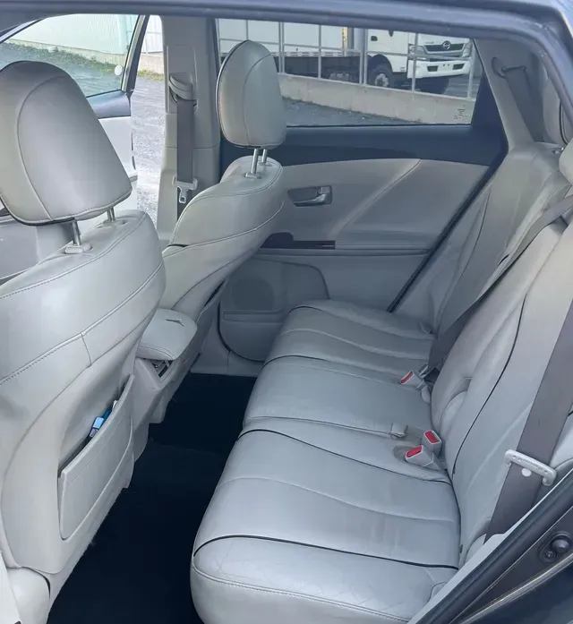 Intérieur des sièges arrière d'une Toyota Venza gris clair. Les sièges sont en cuir, avec les ceintures de sécurité visibles.