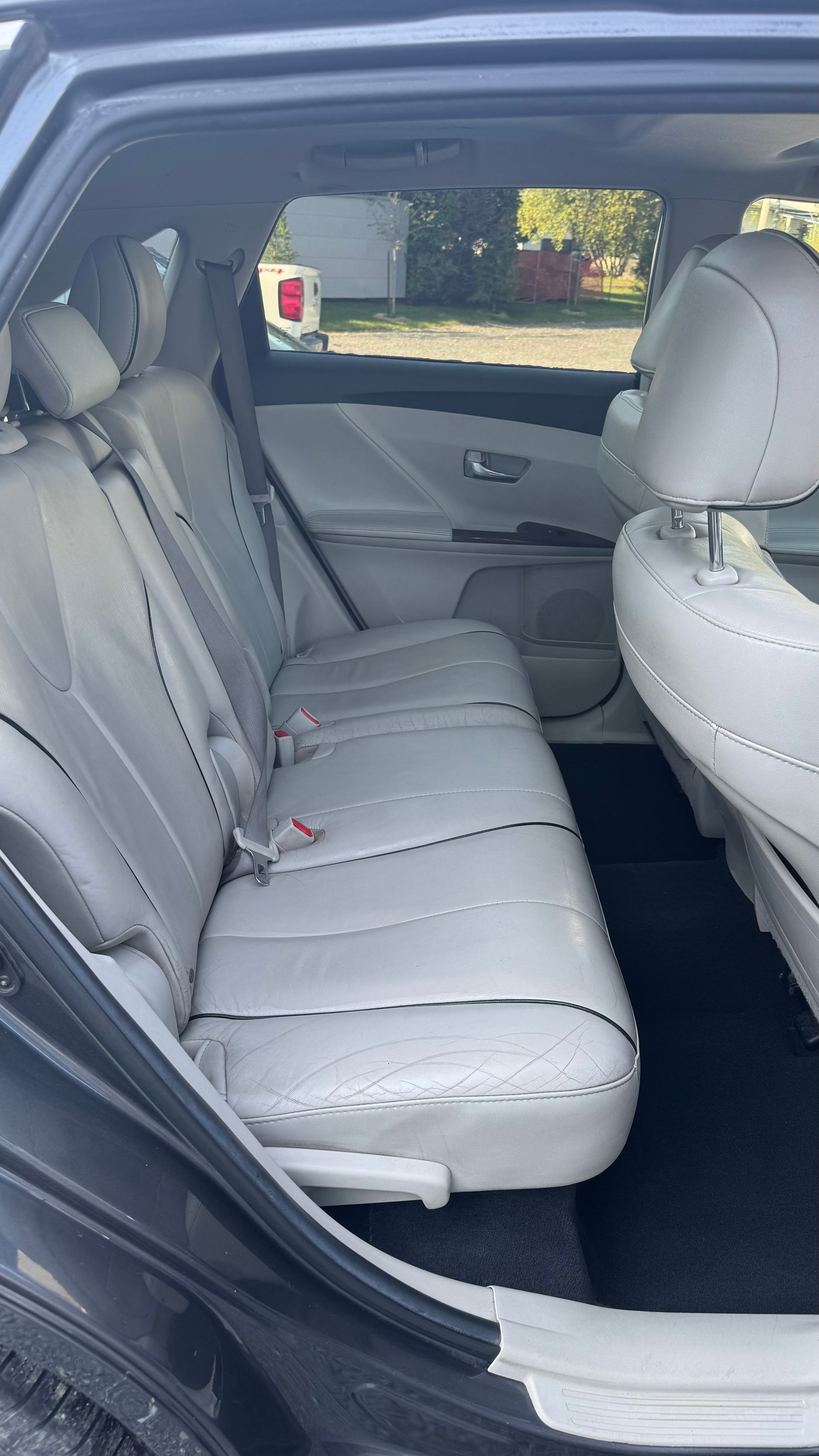 Intérieur arrière d'une voiture grise avec sièges en cuir gris clair ; porte arrière ouverte.