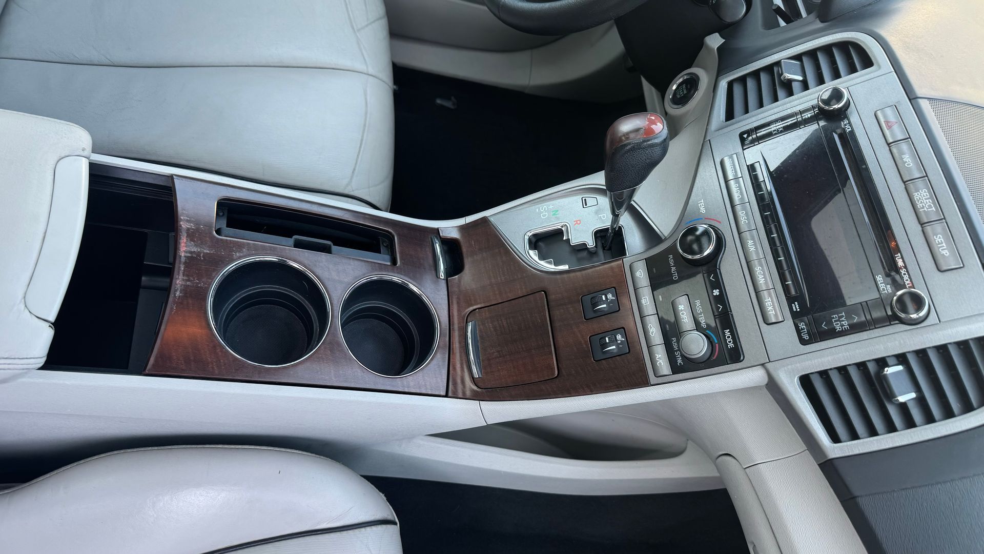 Console centrale de voiture avec finitions en bois. Comprend des porte-gobelets, un levier de vitesse, un écran d'affichage et des aérations.