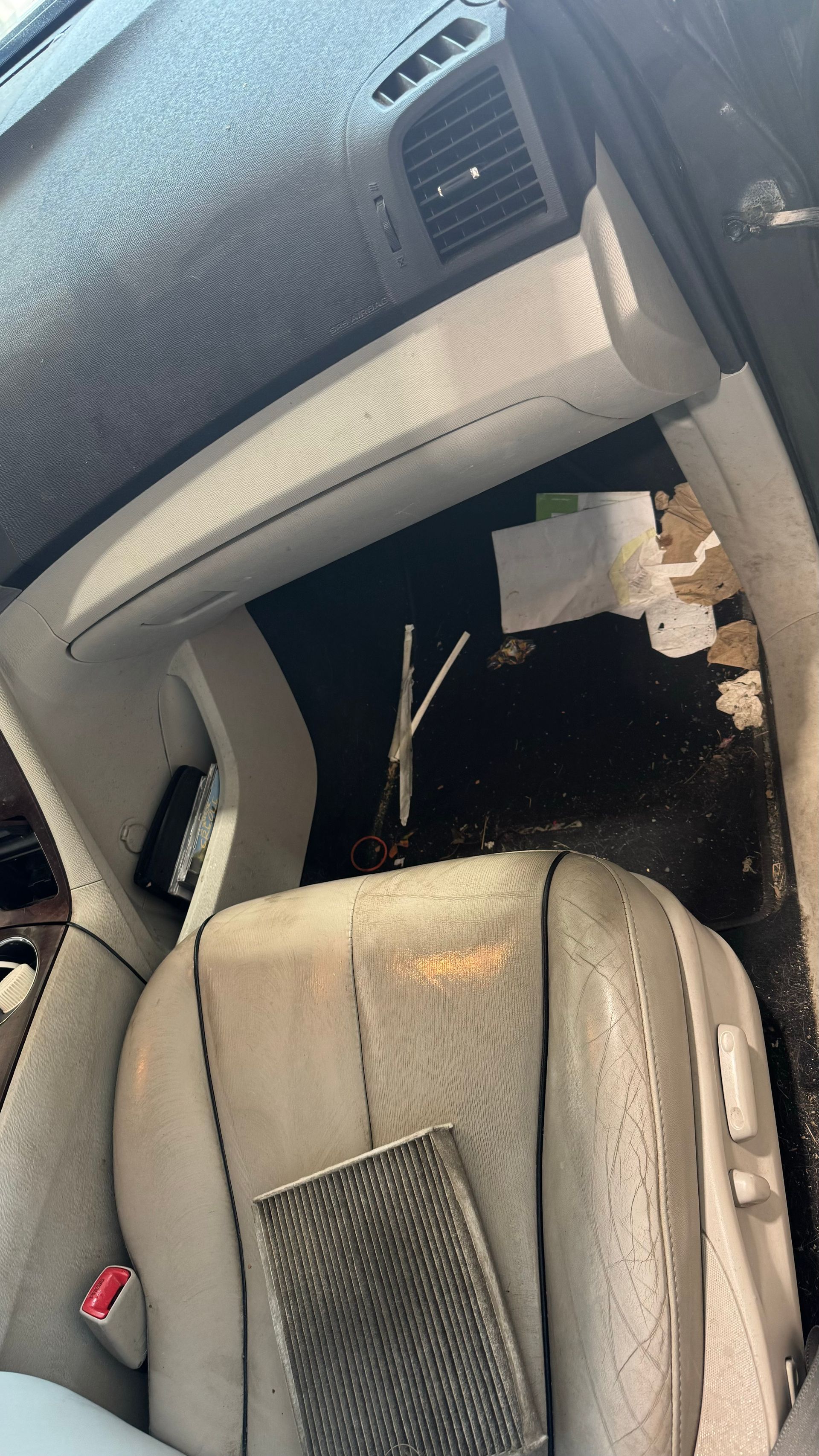 Vue intérieure de la voiture : boîte à gants ouverte, tableau de bord endommagé, sièges sales.