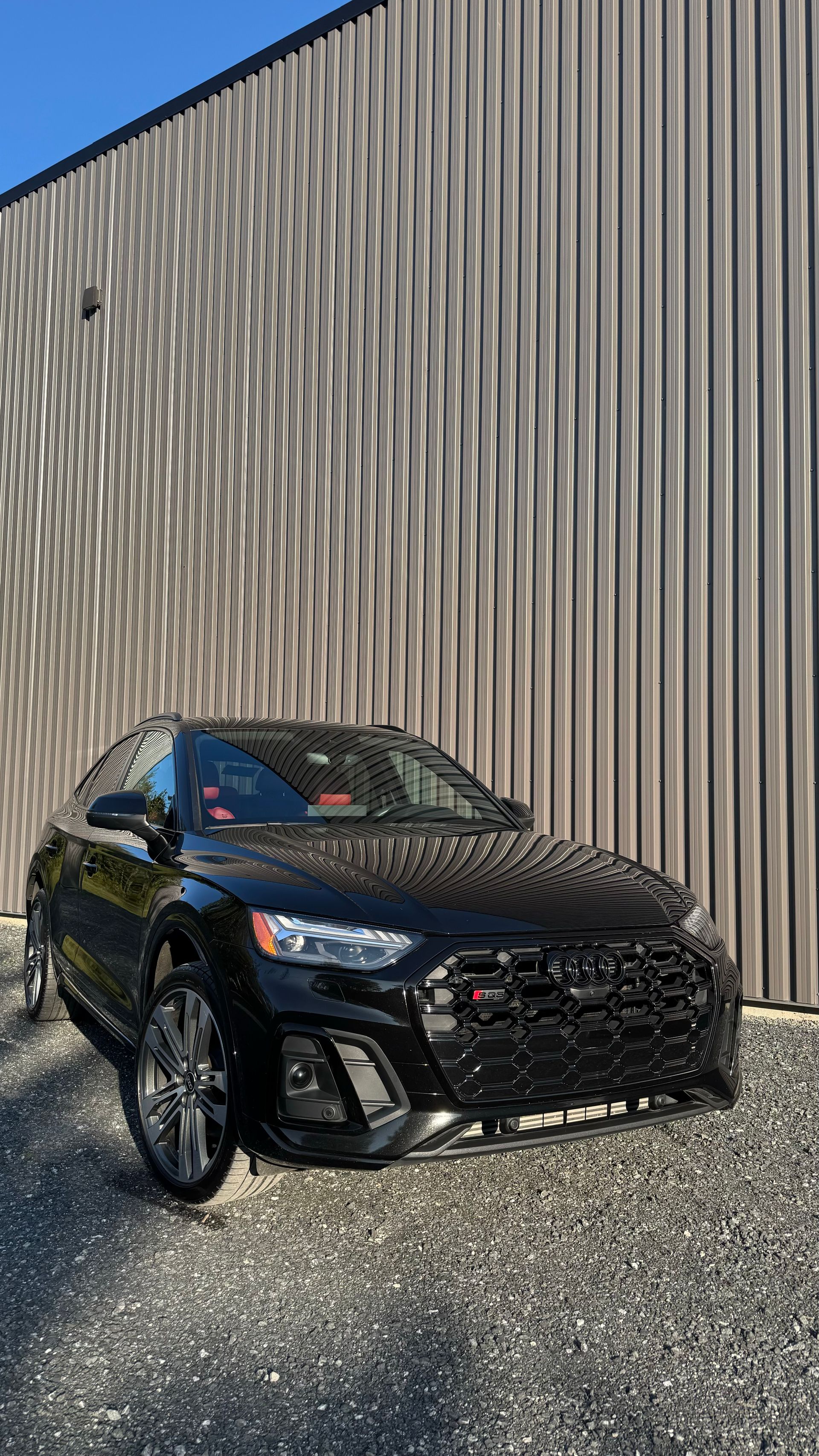 Berline Audi noire garée à l'extérieur d'un bâtiment avec des panneaux argentés texturés.