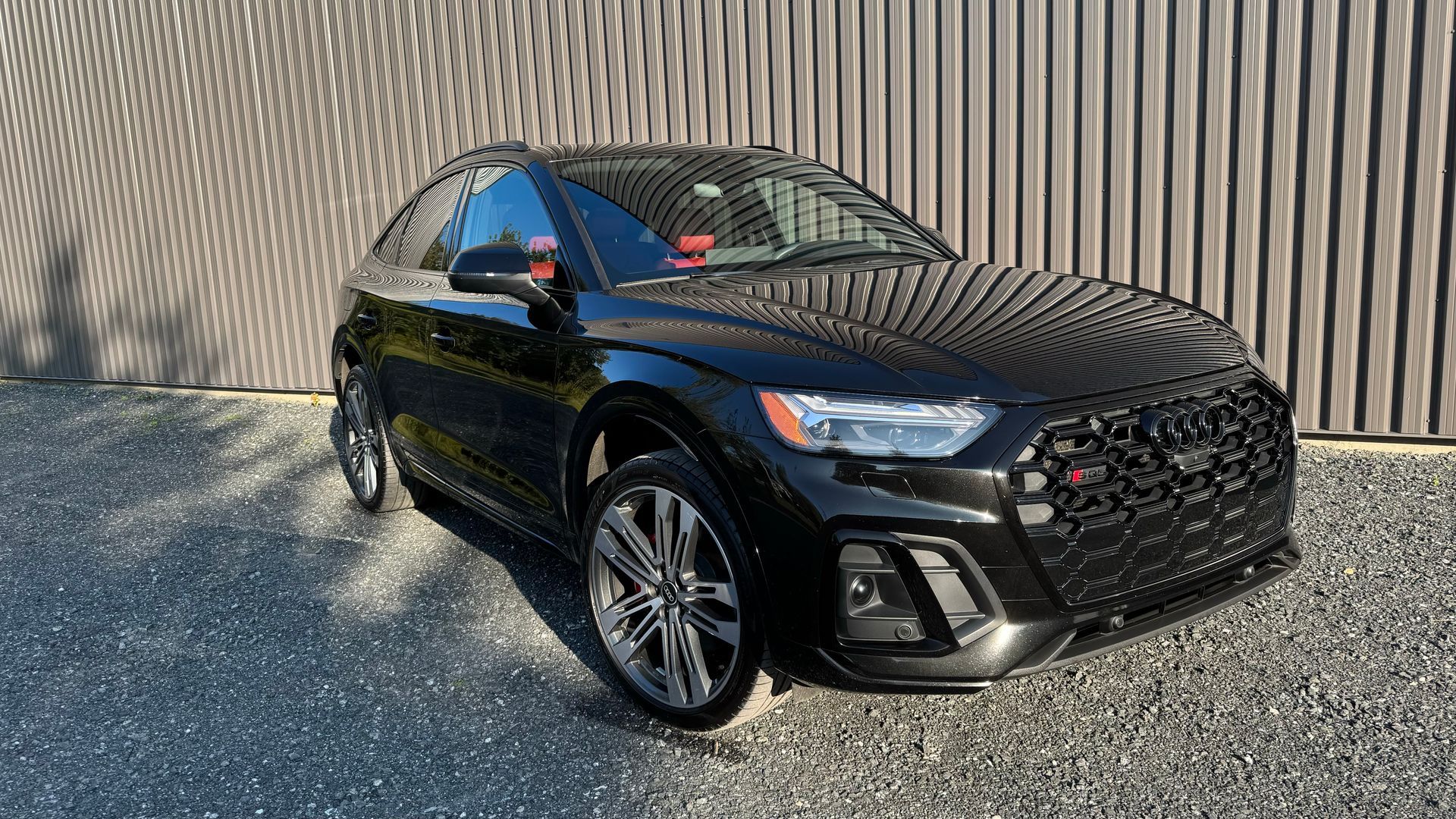 SUV Audi noir garé devant un mur en bois, avec la lumière du soleil à l'avant.