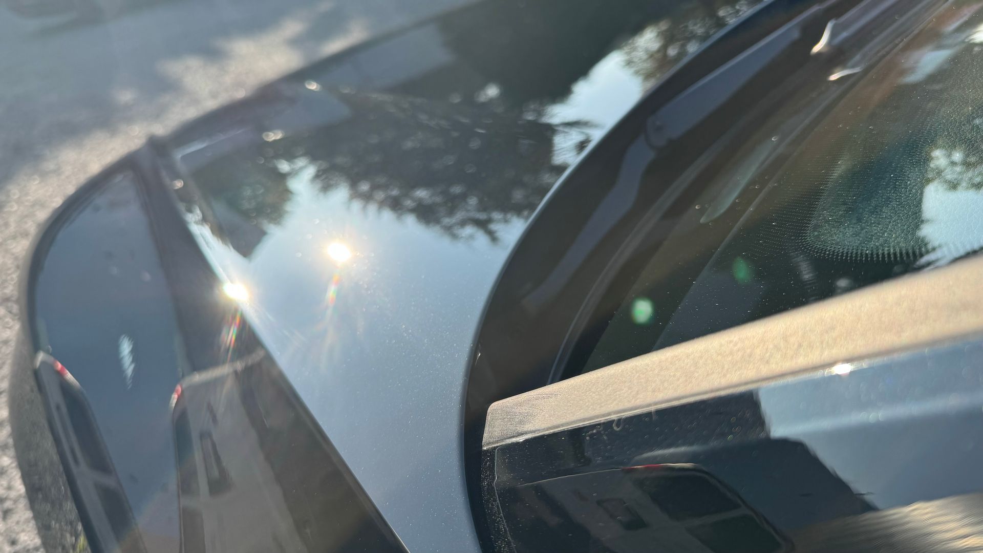 Gros plan d'une voiture gris foncé reflétant la lumière du soleil, garée dans une rue.