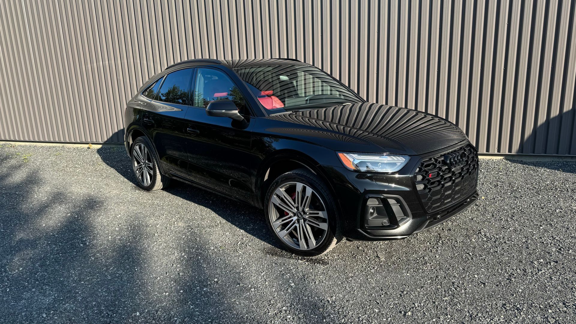 SUV Audi SQ5 noir garé sur du gravier devant un bâtiment gris.
