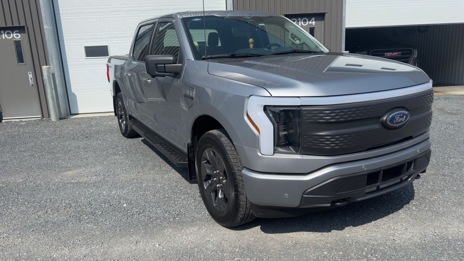 Camion Ford F-150 Lightning gris garé à l'extérieur d'un bâtiment avec une porte blanche et un panneau noir.