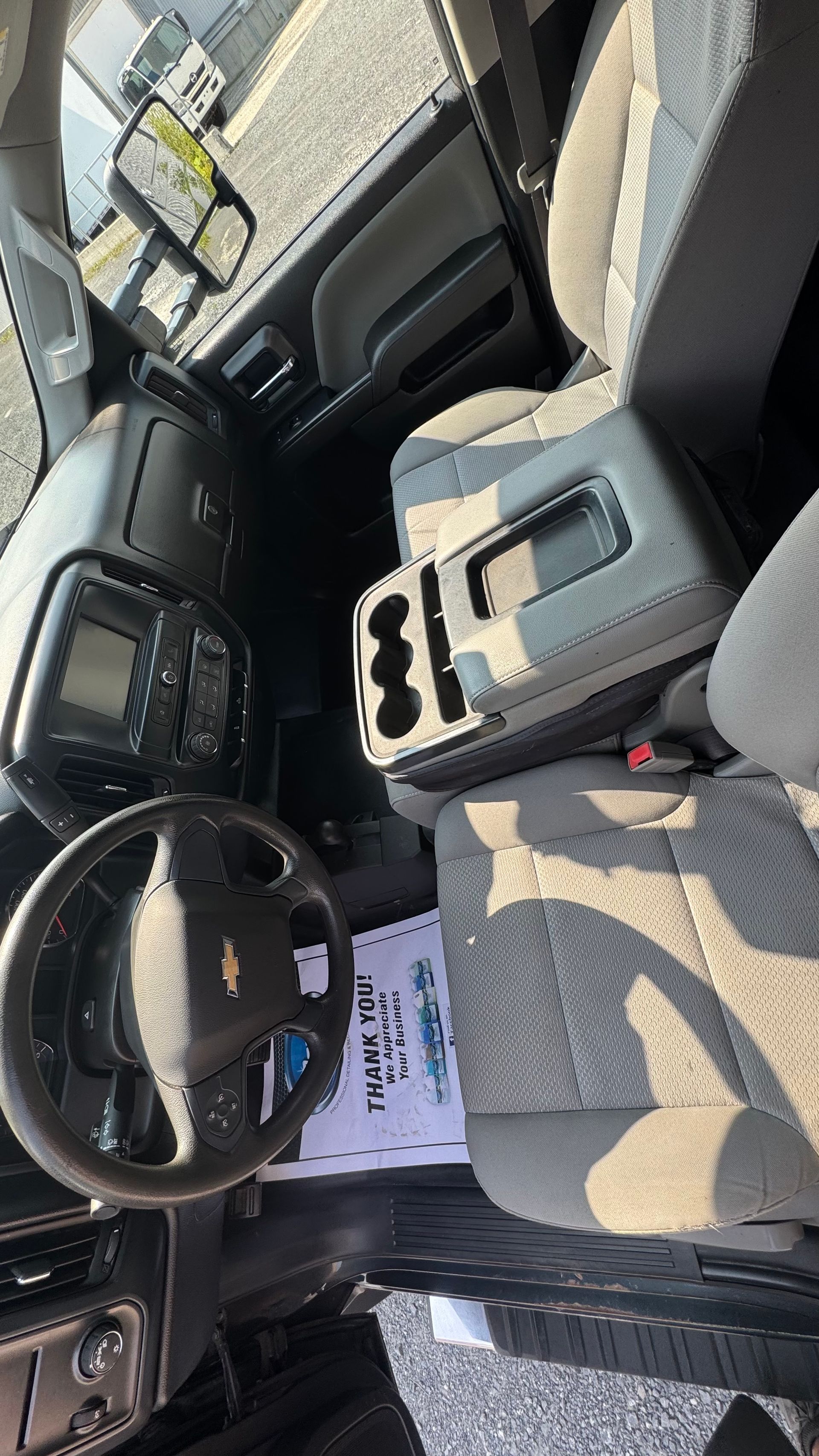 Intérieur d'un camion : volant, console centrale avec porte-gobelets, sièges gris et tableau de bord.