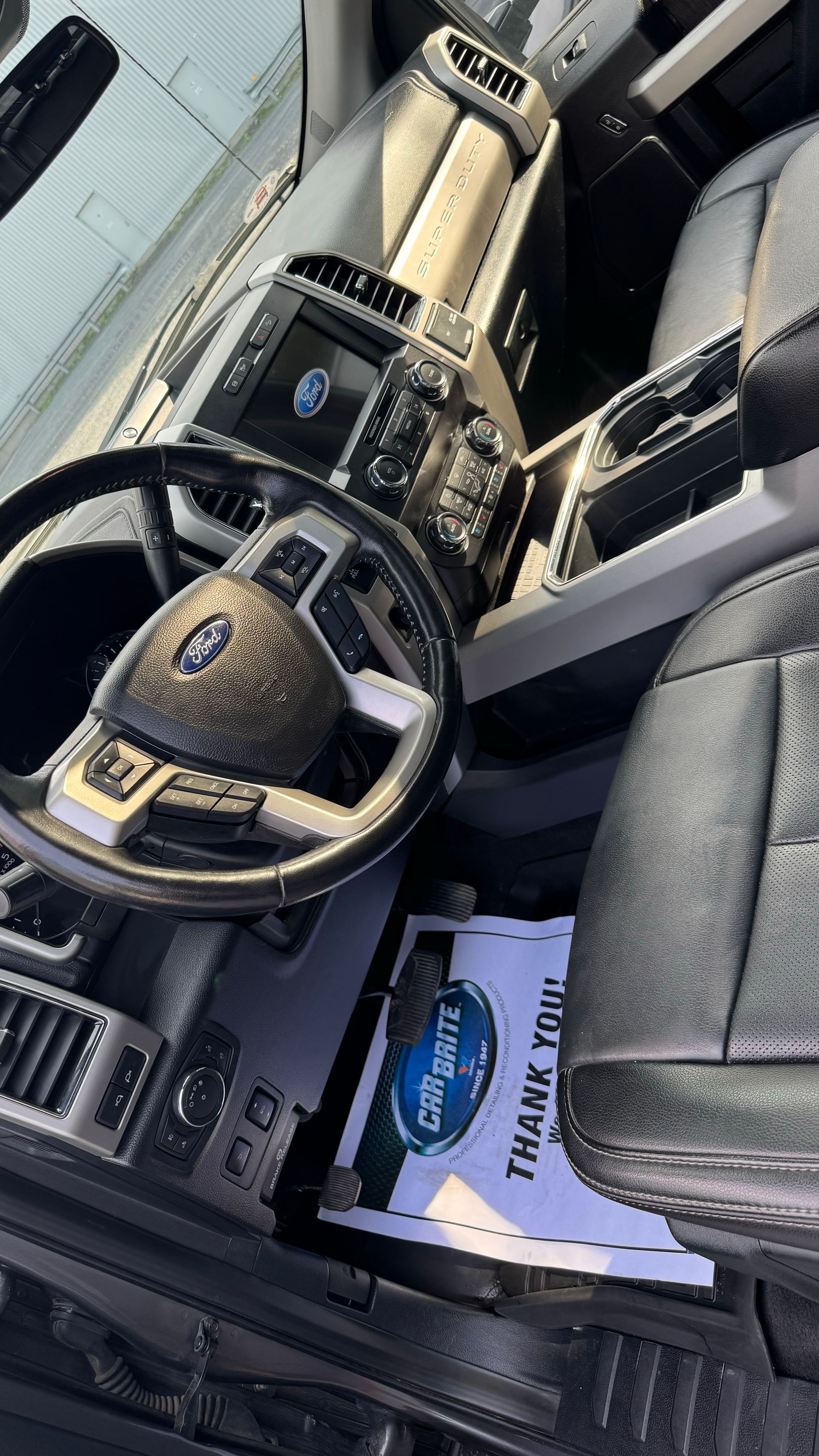 Intérieur d'un camion Ford, avec volant, tableau de bord et sièges. Un tapis de service « Thank You » est visible.