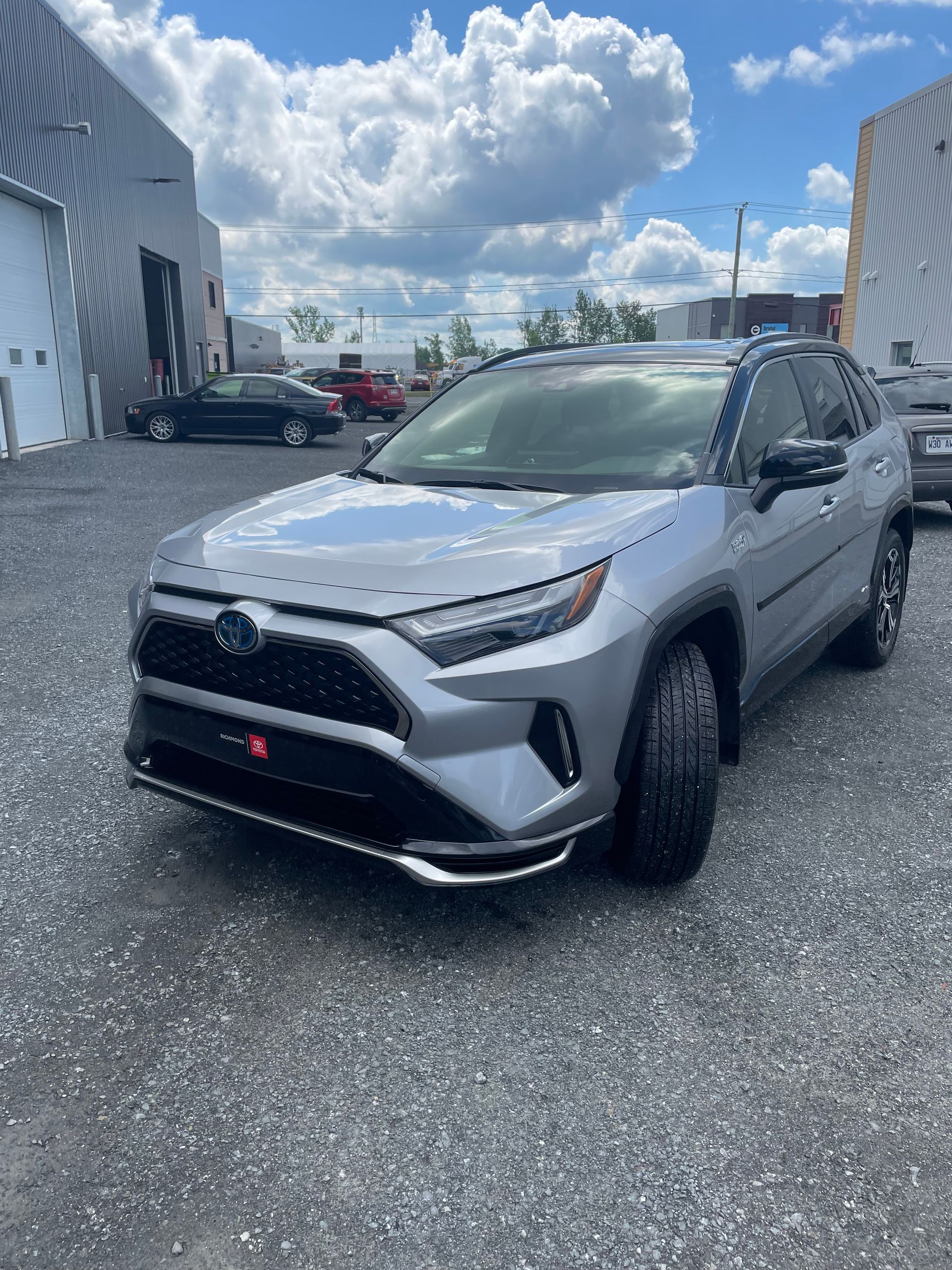 Toyota RAV4 Hybride argenté garé sur l'asphalte, avec un bâtiment et un ciel bleu en arrière-plan.