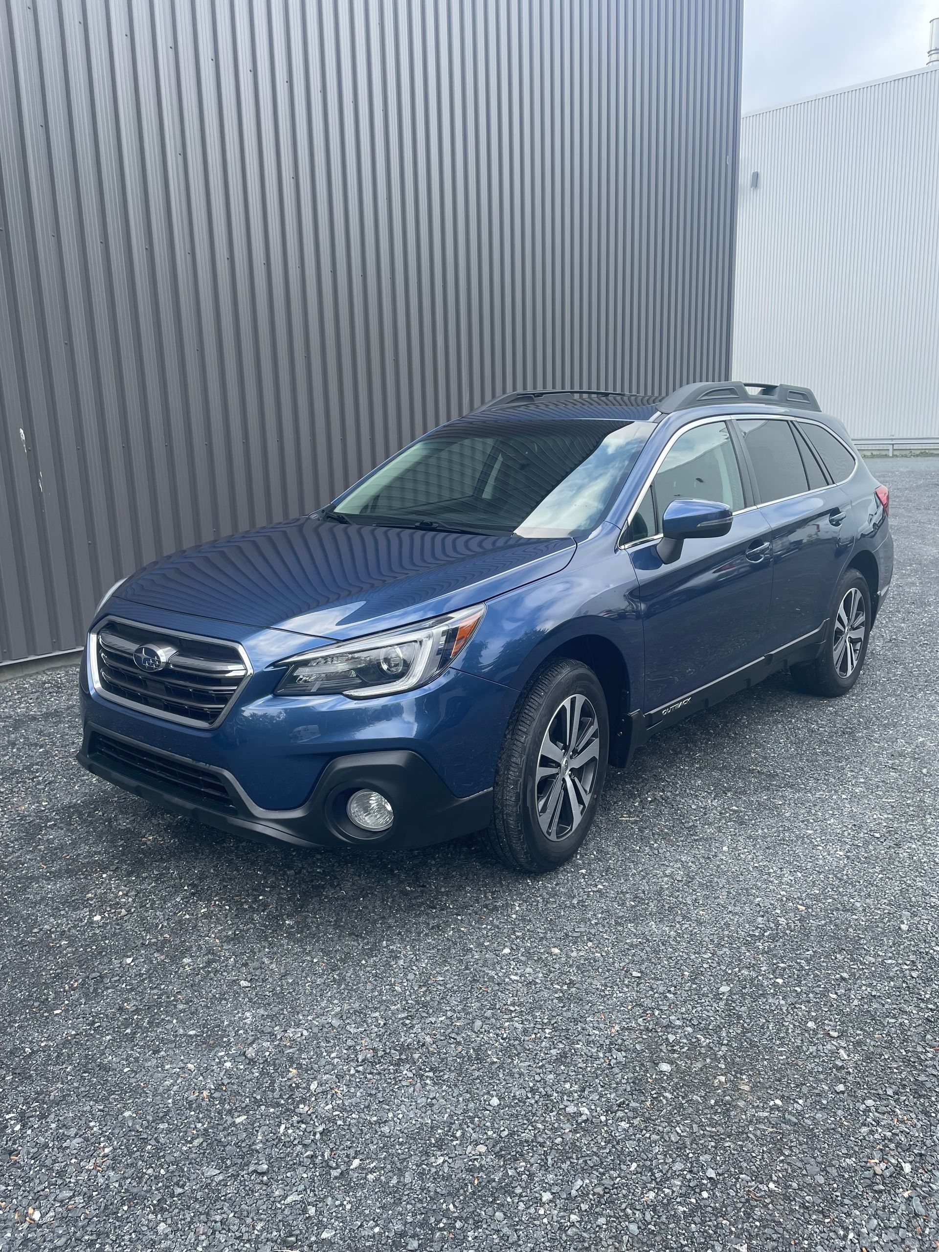 Subaru Outback bleue garée sur du gravier devant un bâtiment gris foncé.