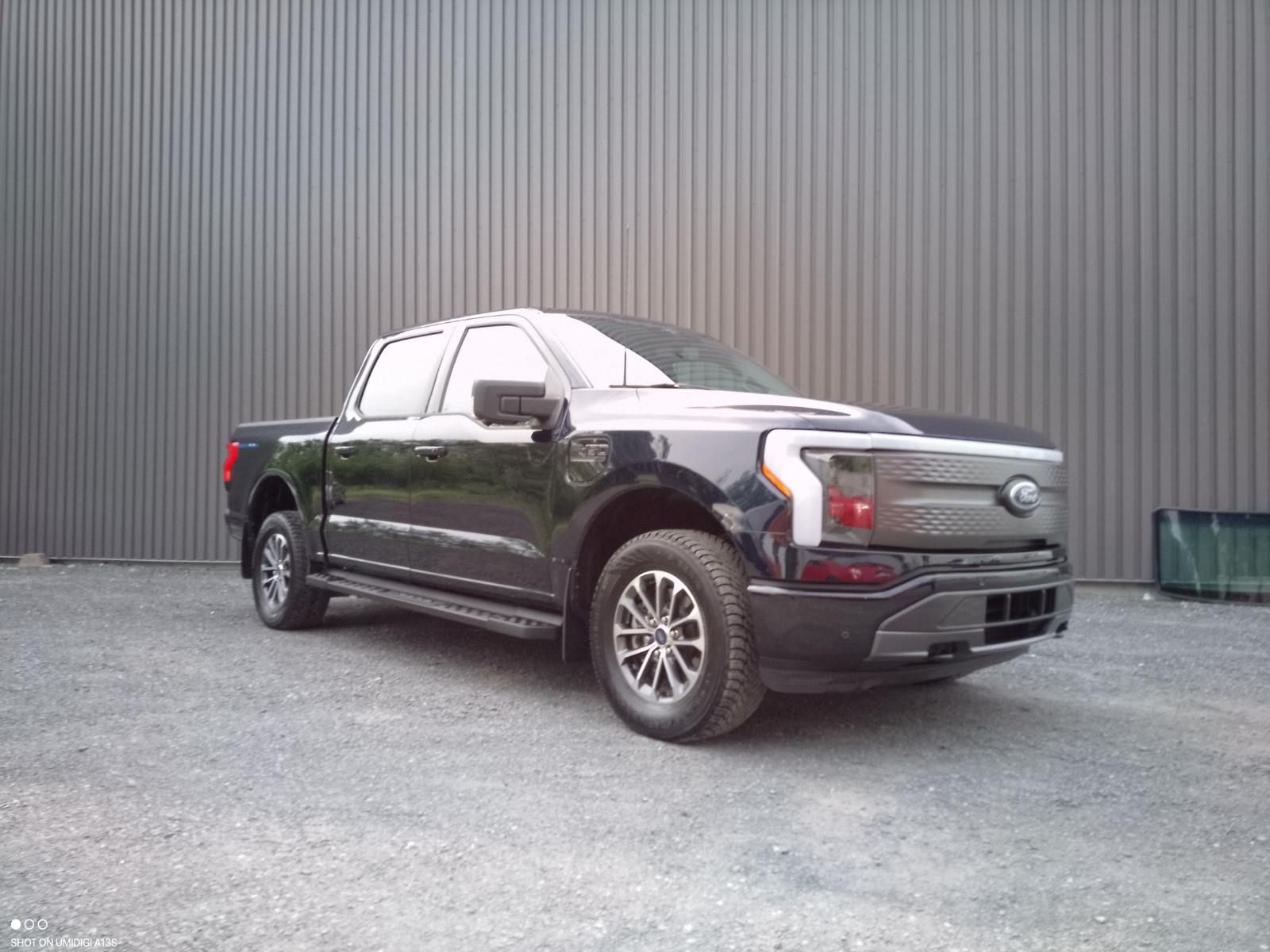 Camionnette électrique Ford F-150 Lightning noire garée devant un bâtiment industriel gris.