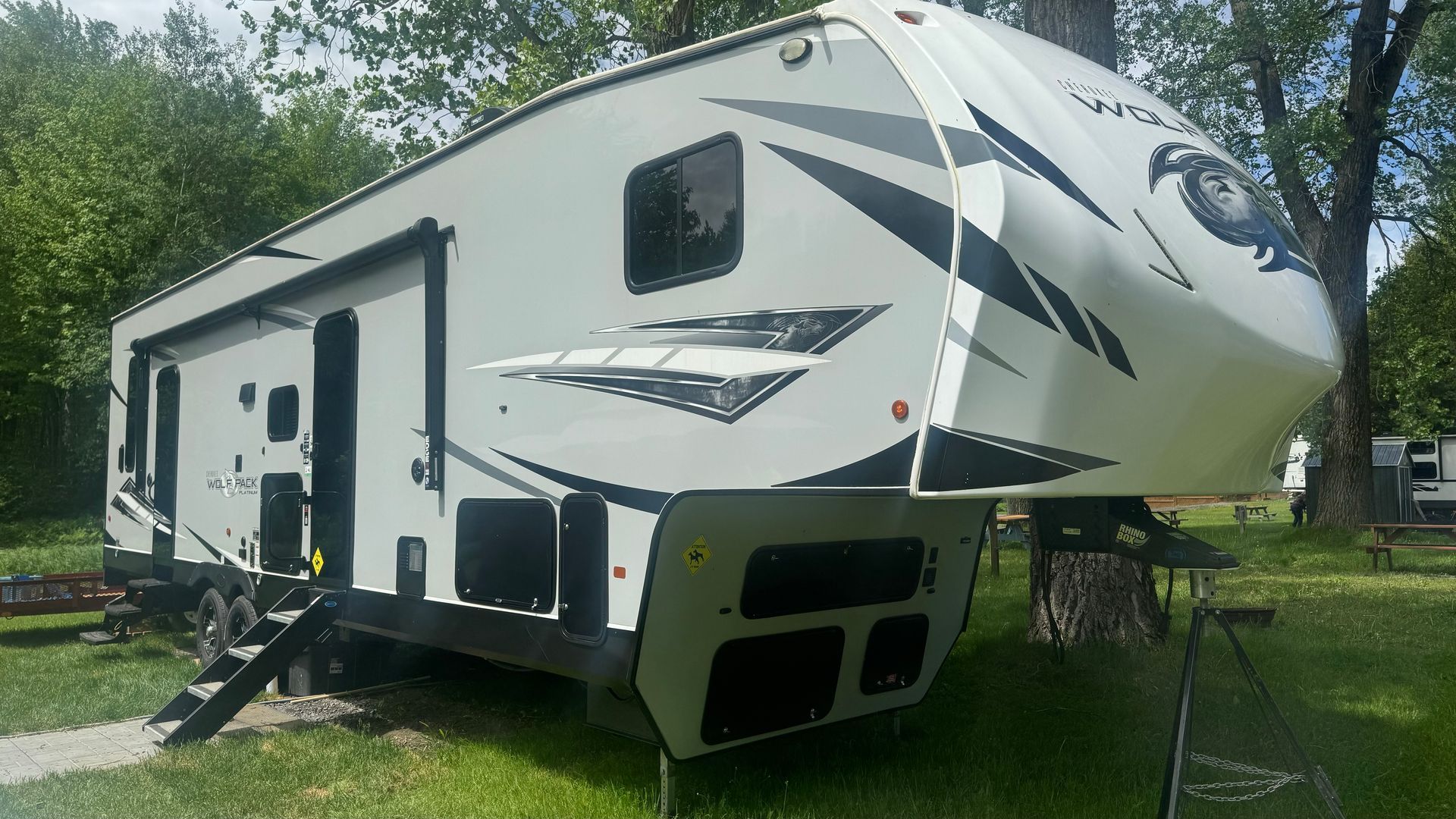 Camping-car blanc et noir stationné sur l'herbe, avec des marches menant à l'entrée, dans un cadre de parc.
