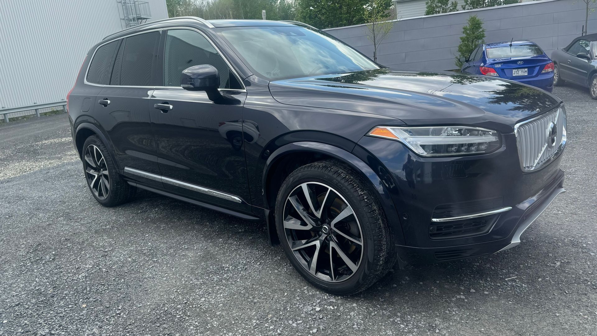 SUV Volvo XC90 bleu foncé garé sur du gravier dans un cadre extérieur.