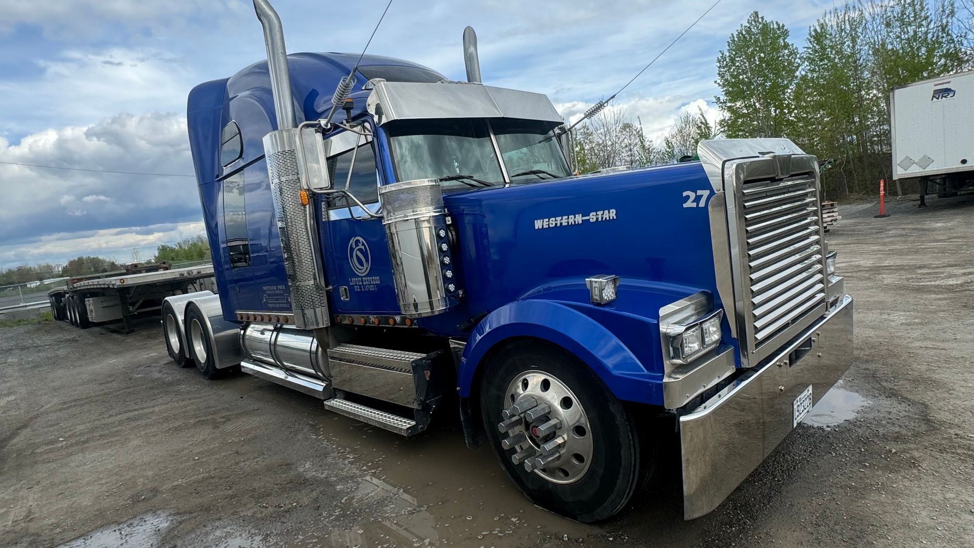 Semi-remorque bleu stationné à l'extérieur. Le camion est doté de touches chromées et d'une remorque à plateau.