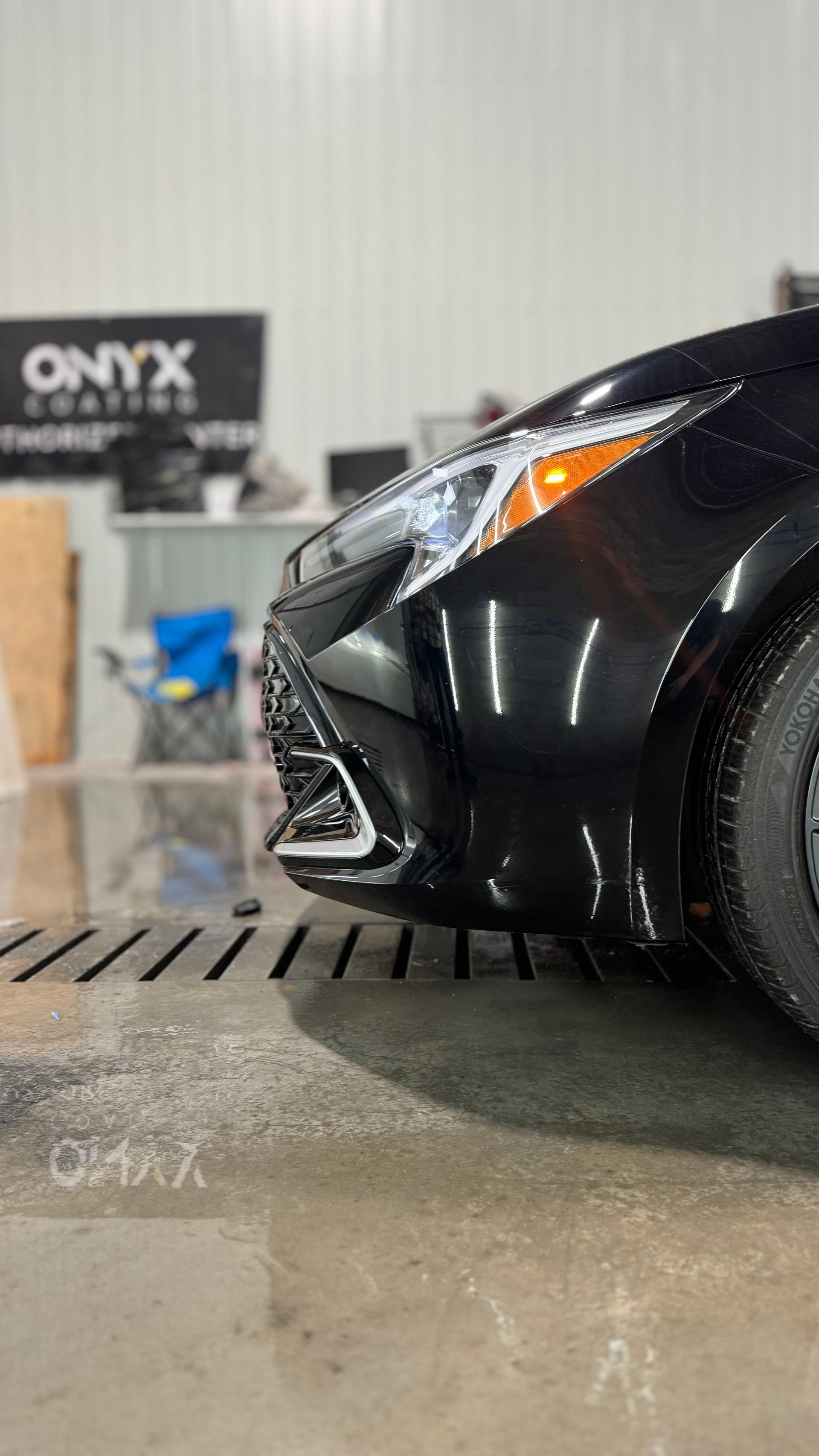 Vue avant d'une voiture noire, sol mouillé, avec le panneau « ONYX COATINGS » en arrière-plan.