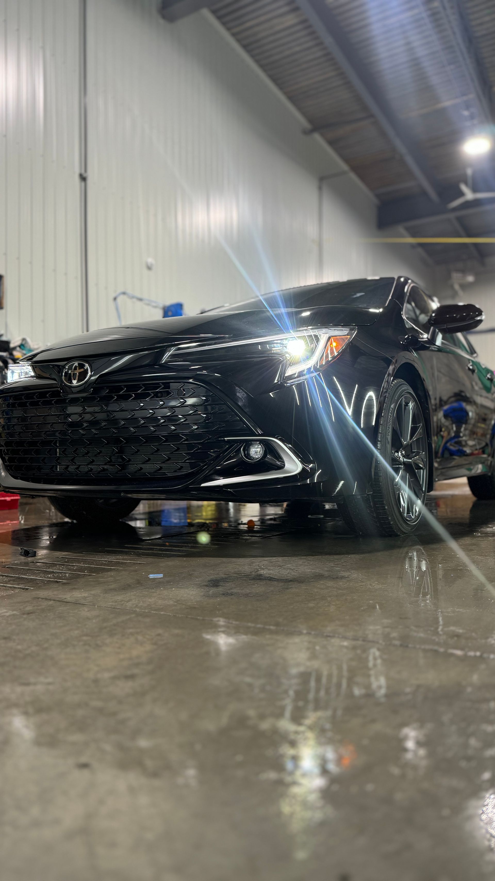 Voiture noire lavée dans un garage, eau savonneuse sur la voiture.