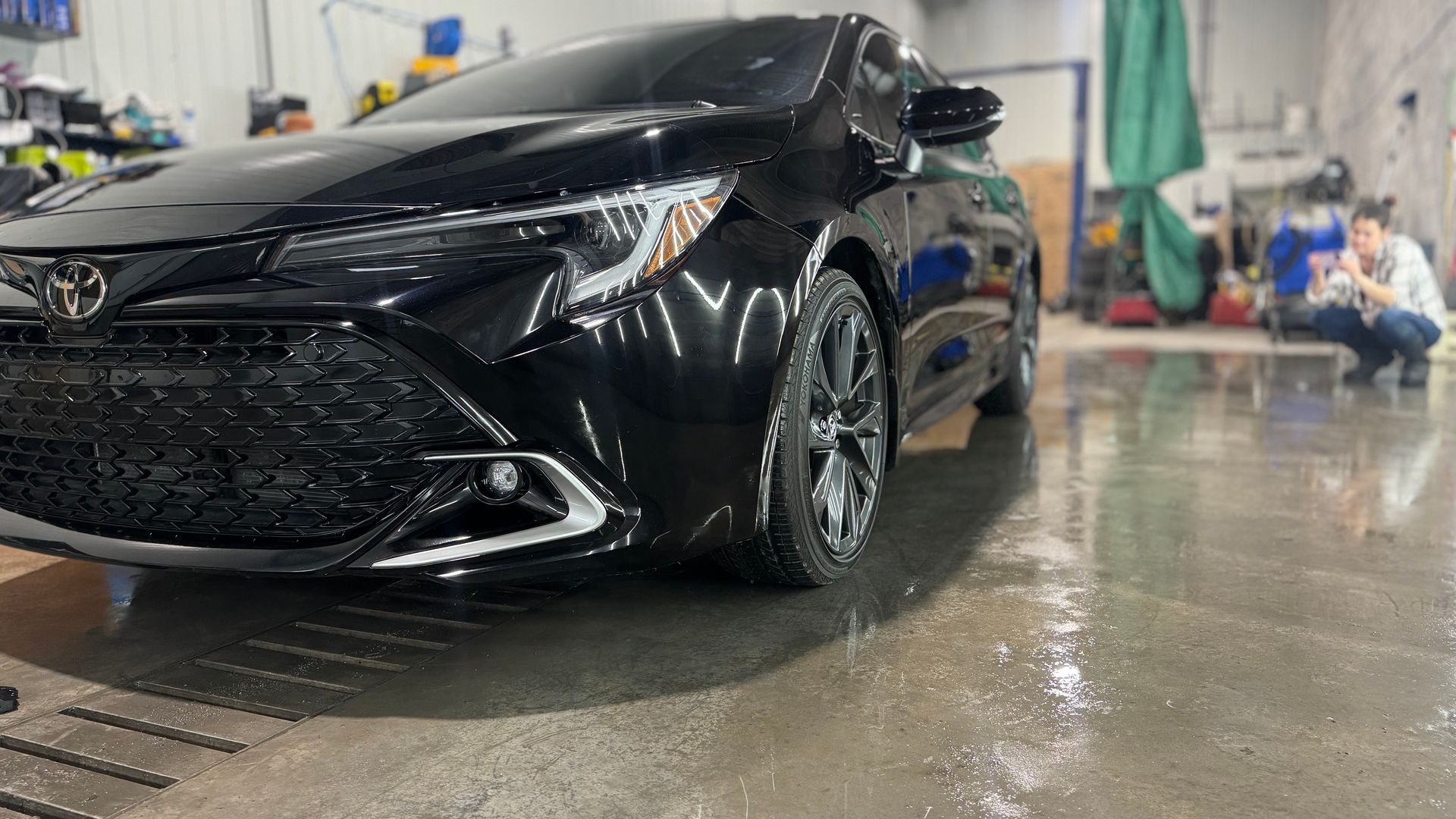 Toyota Corolla noire dans un lave-auto, la chaussée mouillée reflète la voiture.