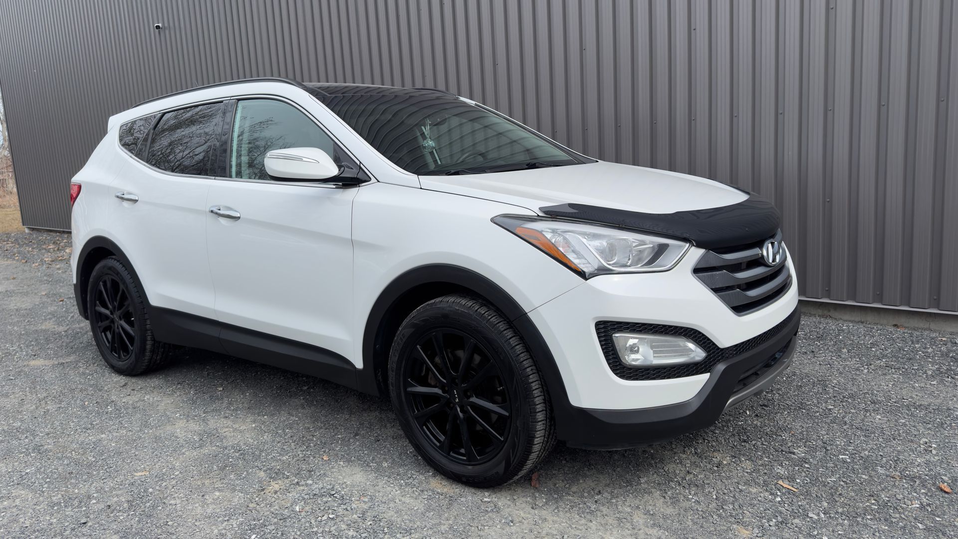 SUV Hyundai Santa Fe blanc avec roues noires garé devant un bâtiment gris.