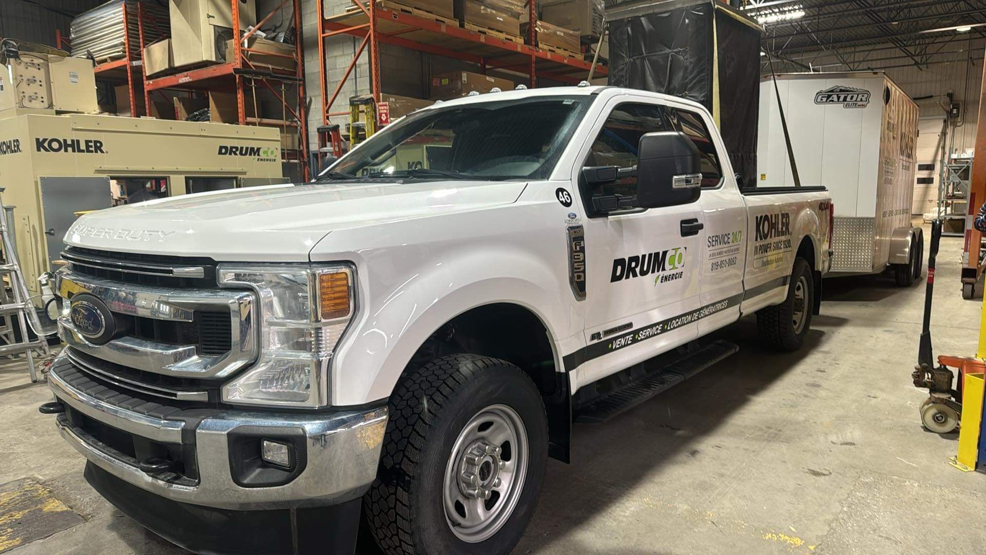 Pick-up Ford blanc tirant une remorque dans un entrepôt. Le logo de l'entreprise est visible sur le côté.