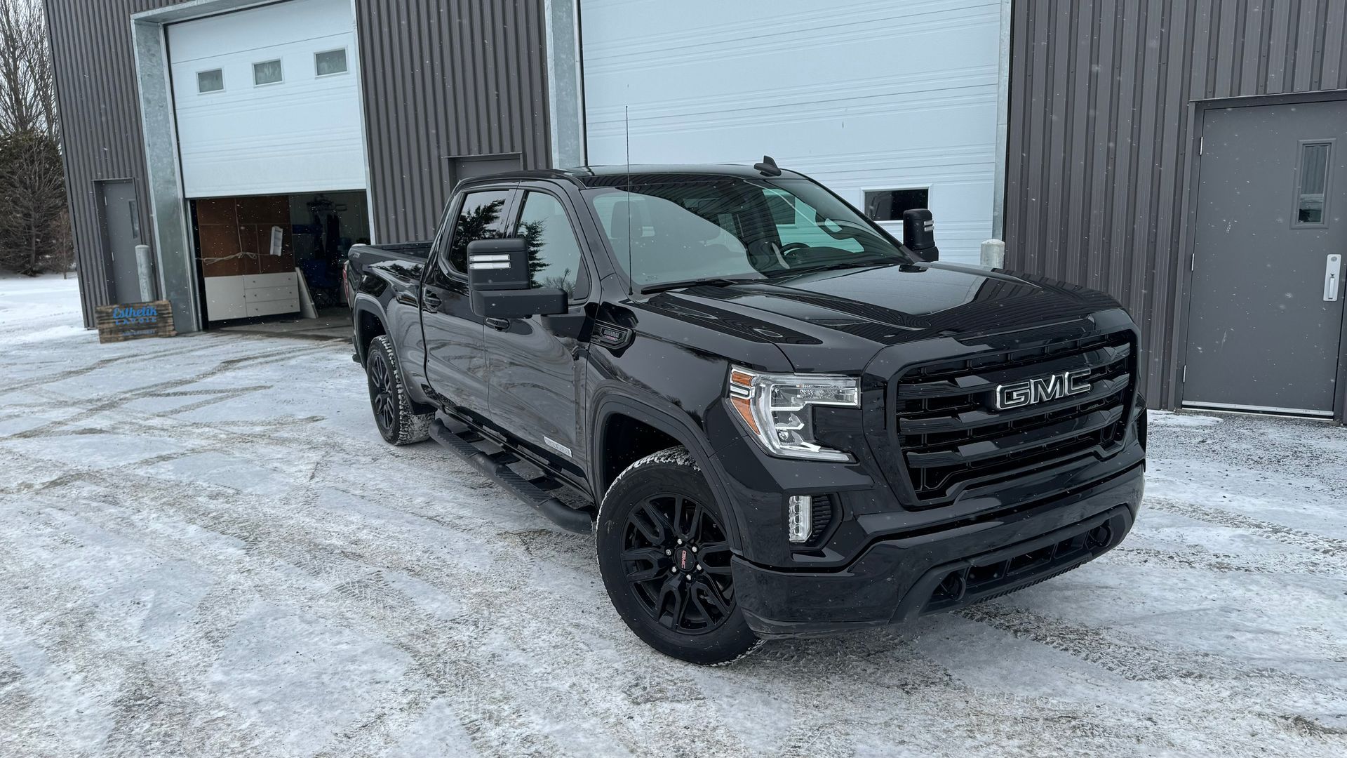 Camionnette GMC Sierra noire stationnée sur un sol enneigé devant un bâtiment.