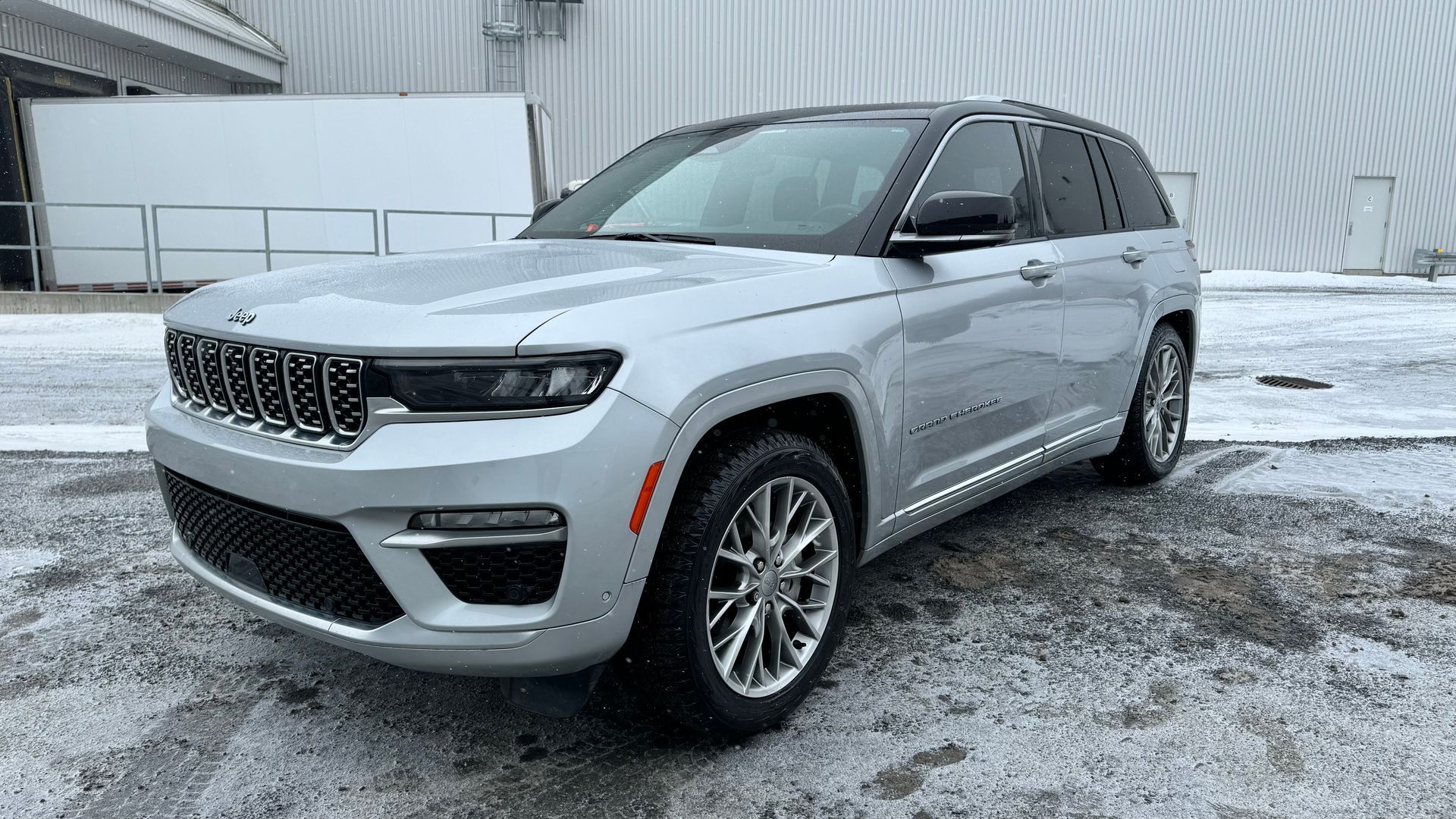 SUV Jeep Grand Cherokee argenté stationné sur une surface enneigée.