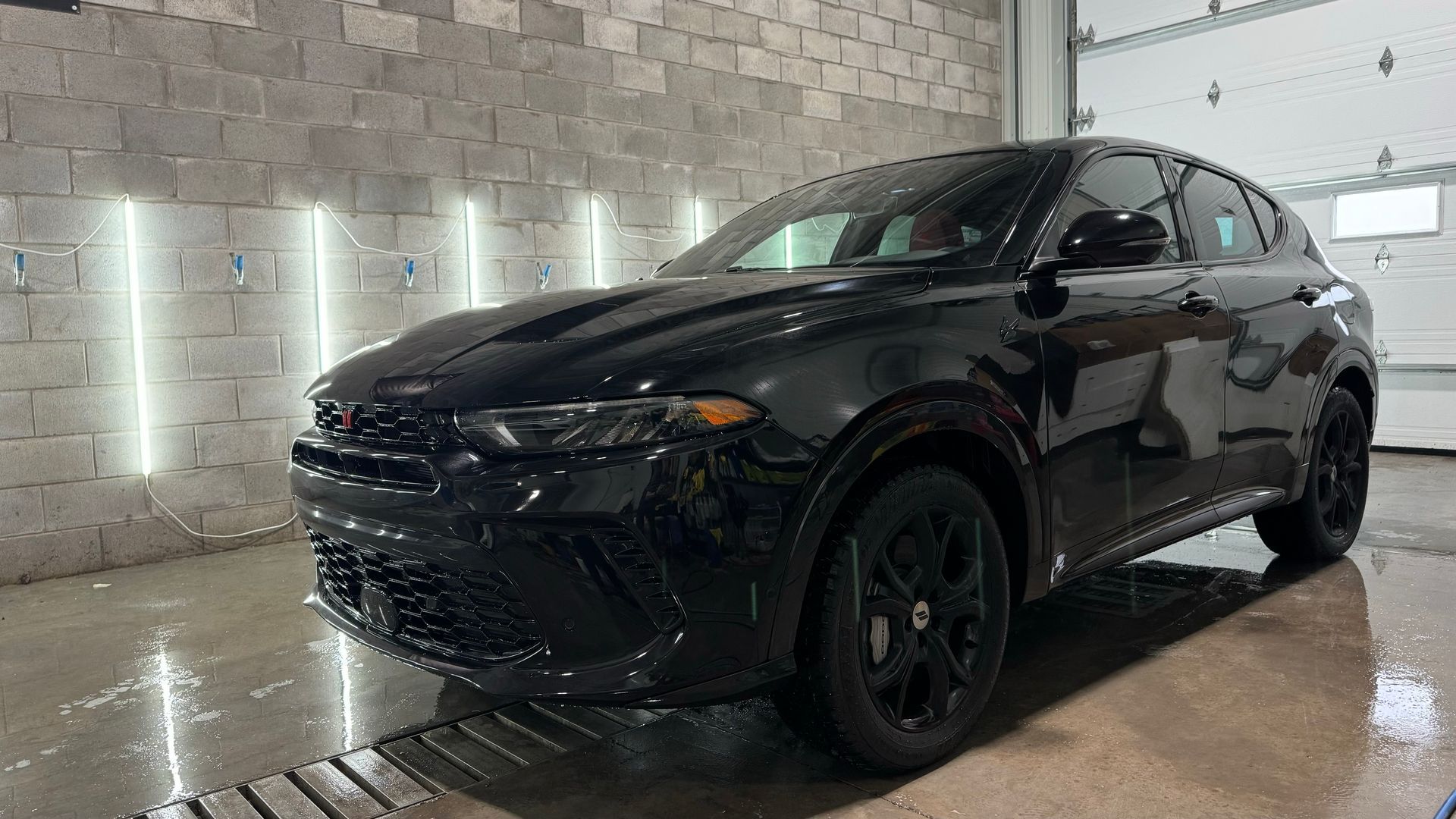 SUV noir dans une baie de lavage de voiture avec trottoir mouillé et mur de briques.
