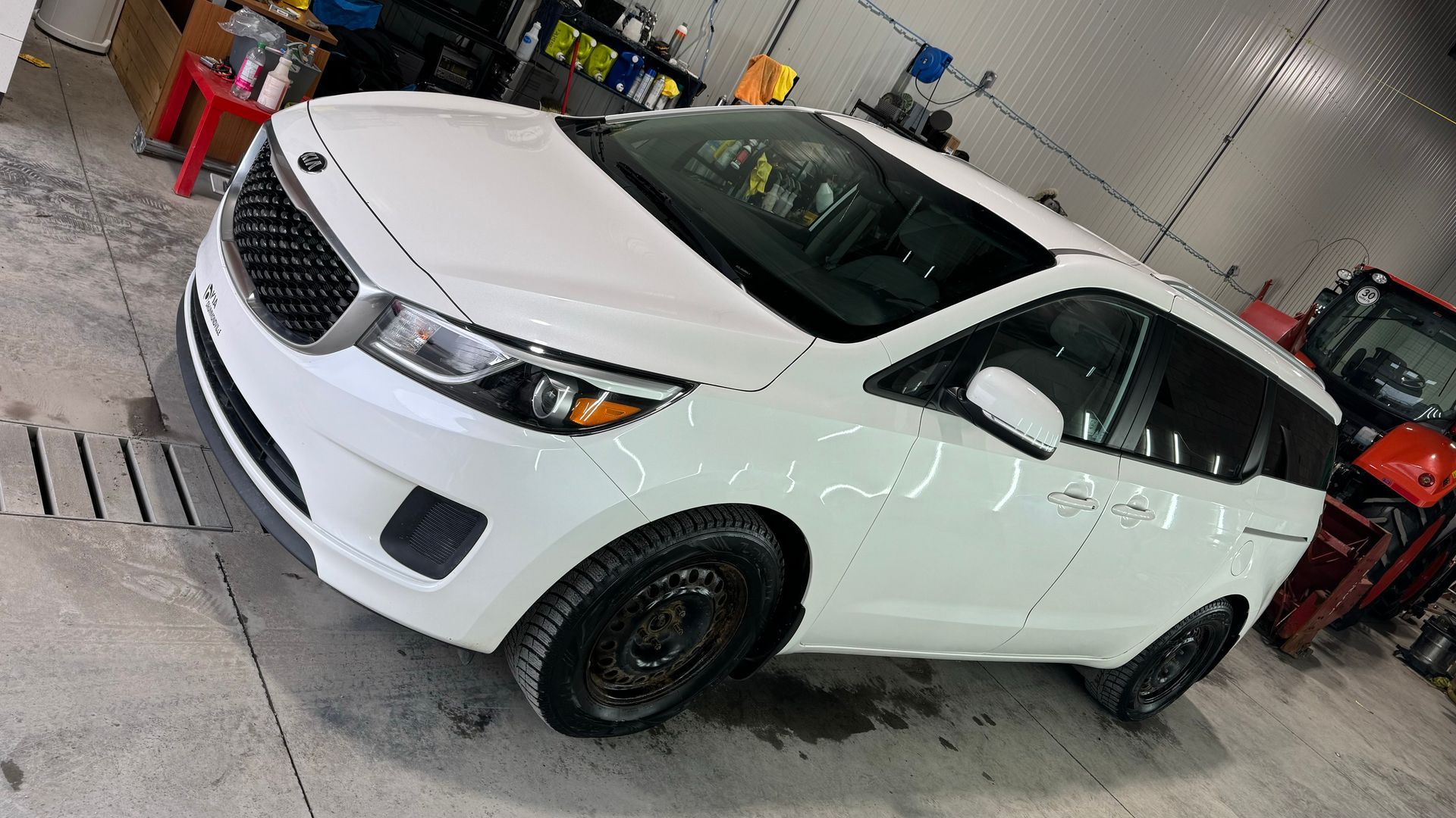 Minifourgonnette Kia blanche garée dans un garage ; jantes foncées.