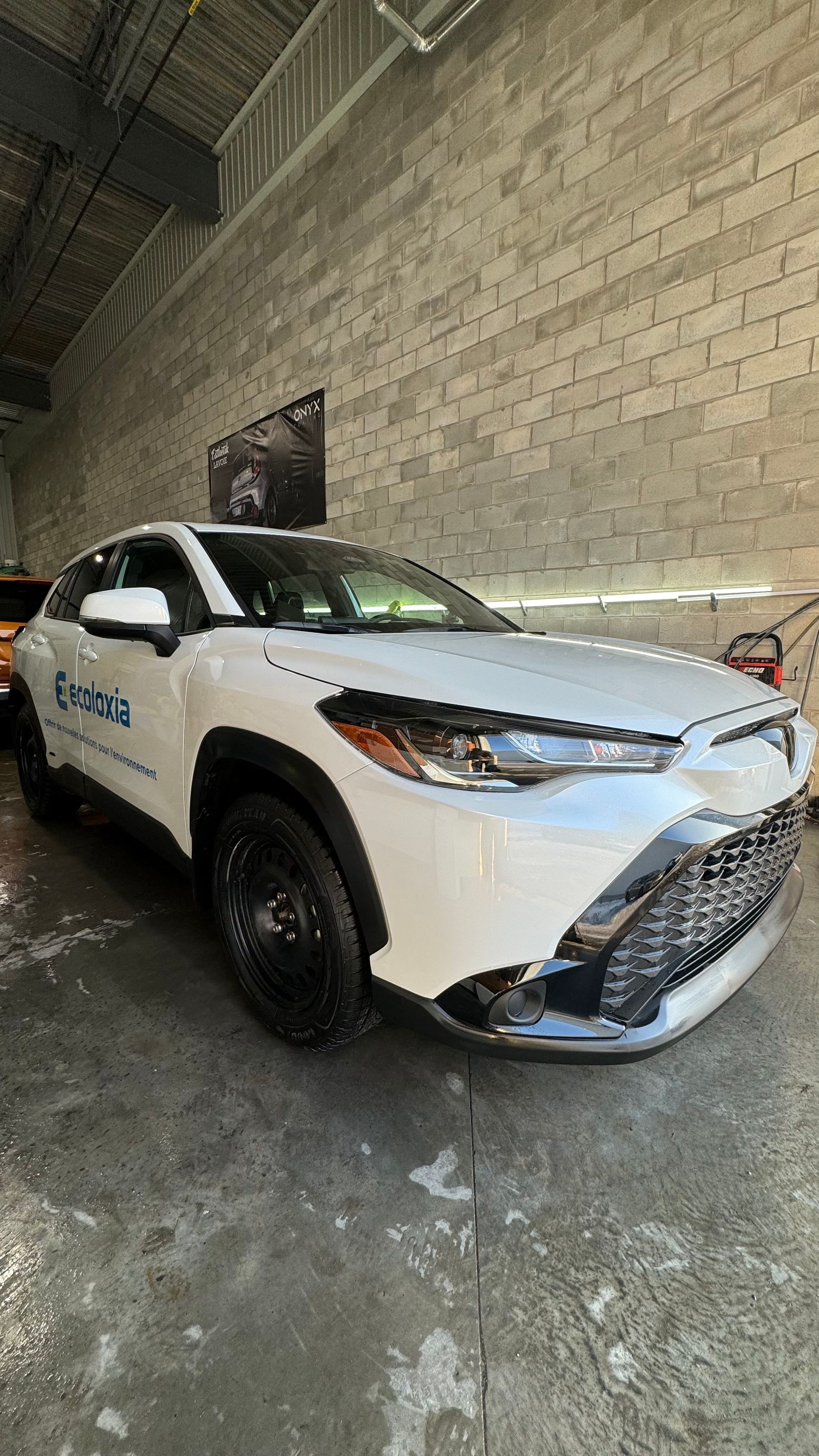 Toyota Corolla Cross blanche garée dans un garage avec un mur de briques.