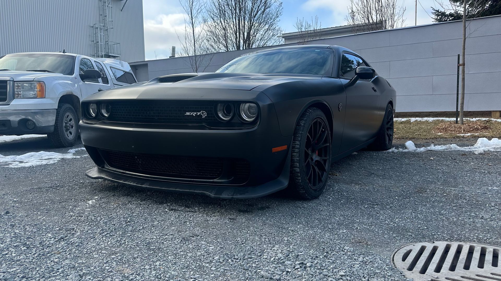 Dodge Challenger noire garée sur du gravier, devant un bâtiment, un jour de neige.