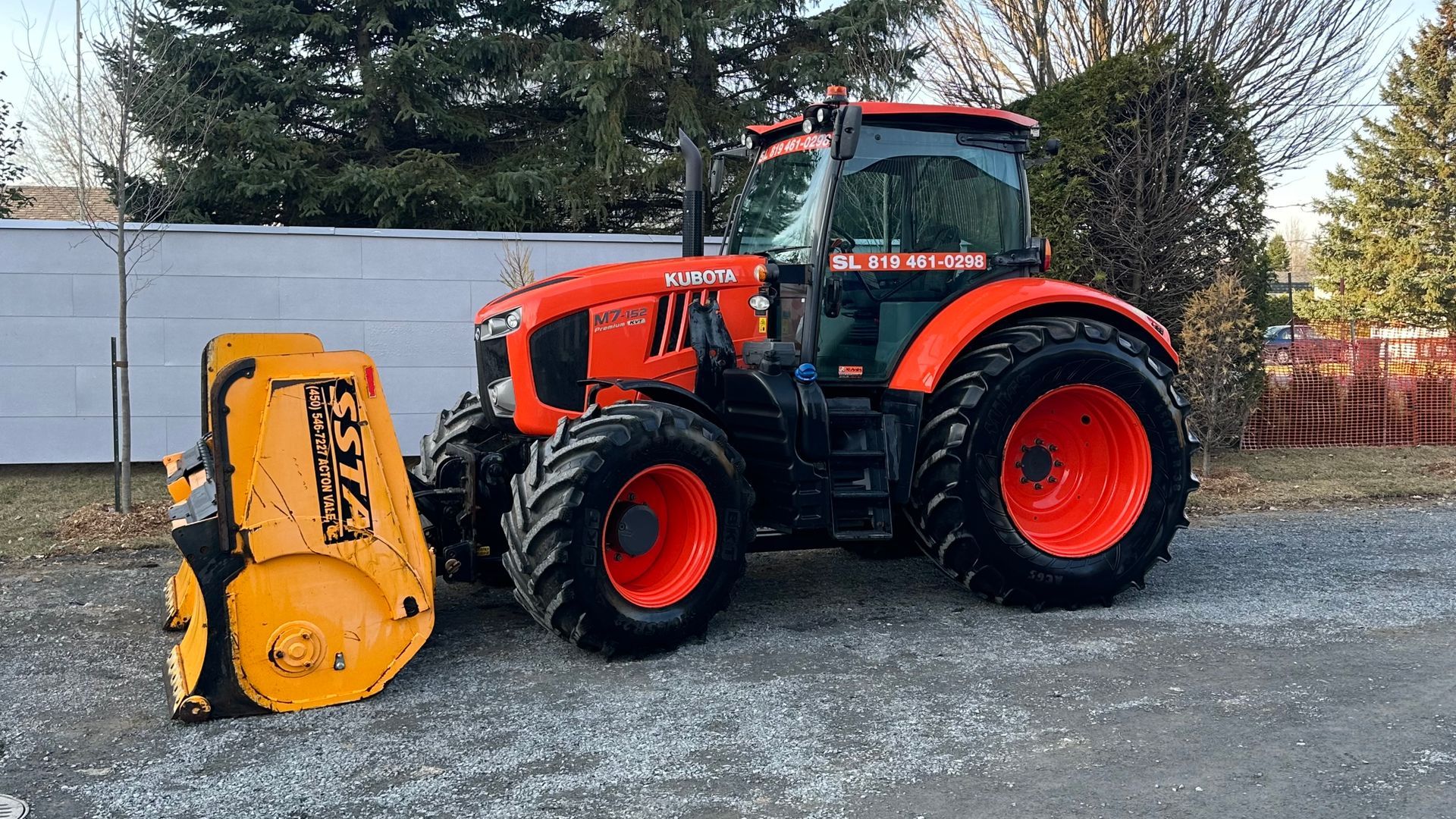 Tracteur Kubota orange avec une souffleuse à neige, stationné dans une allée.