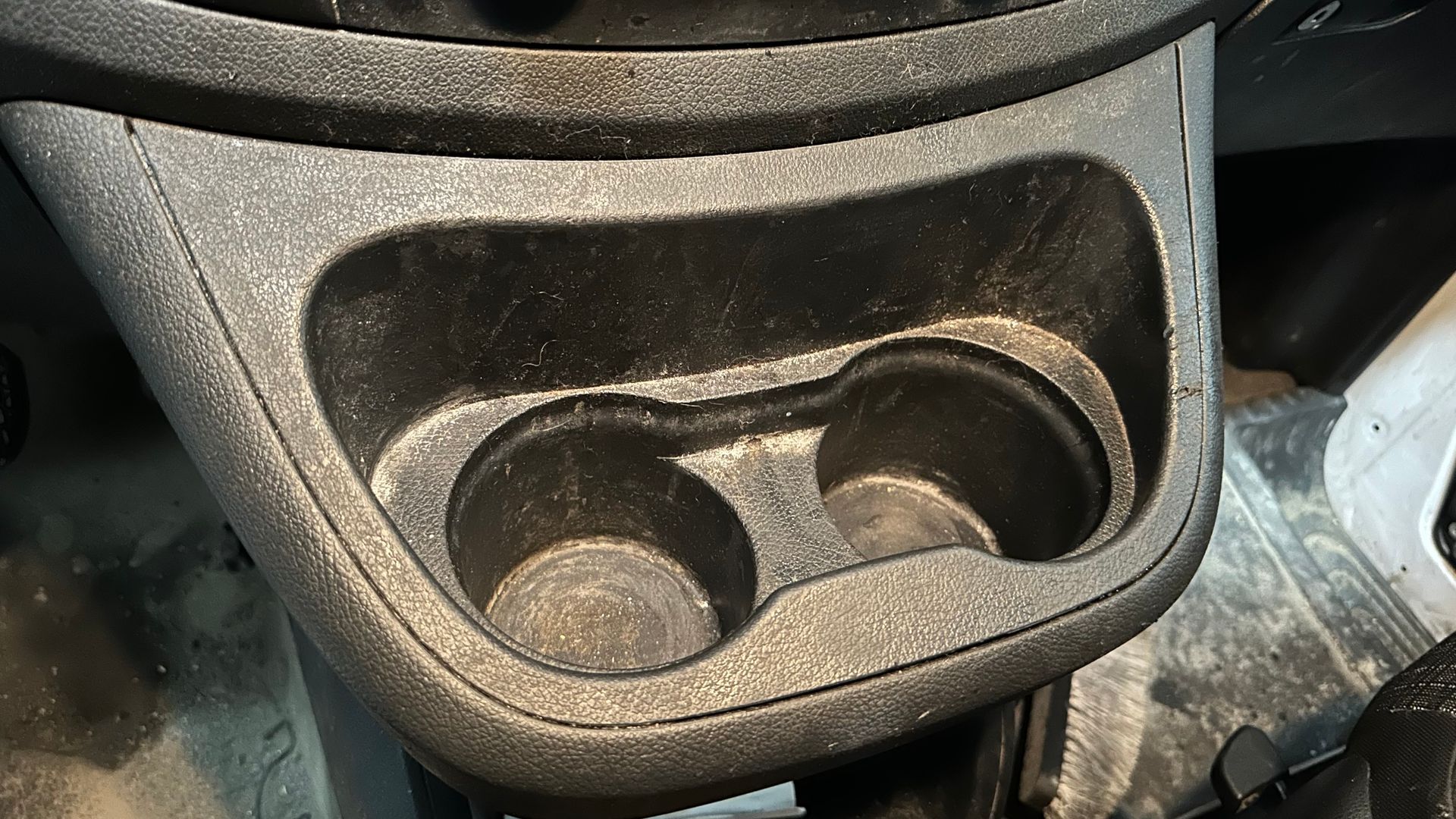 Porte-gobelet texturé noir pour voiture avec deux compartiments circulaires, intérieur poussiéreux.