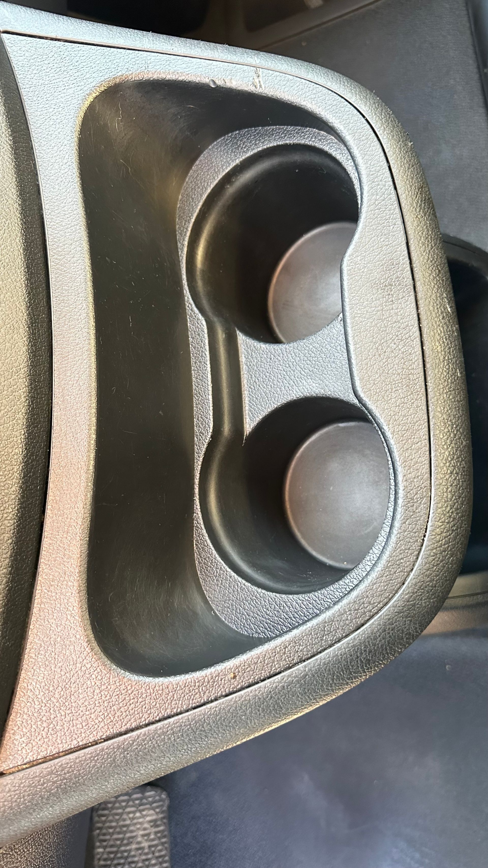 Console de voiture noire avec deux porte-gobelets, légèrement poussiéreuse.