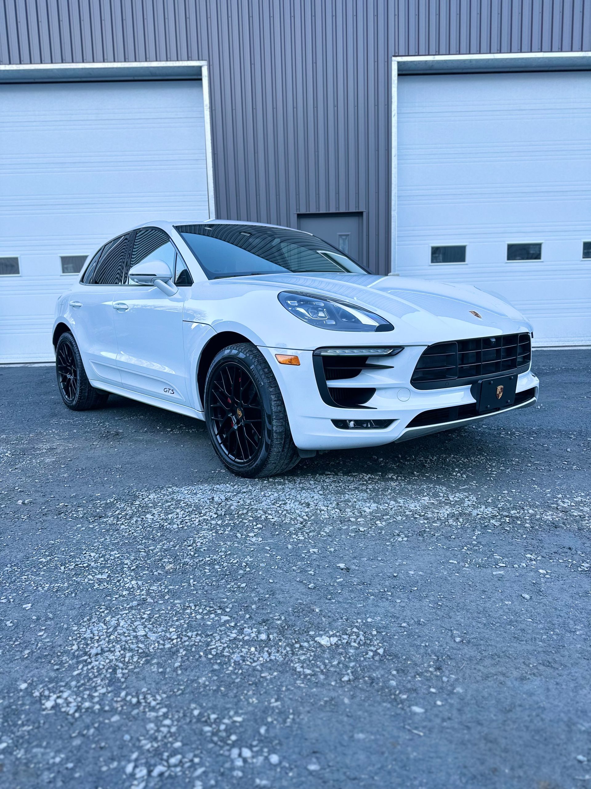 Un SUV Porsche blanc garé devant un immeuble avec des portes de garage blanches. Jantes noires.
