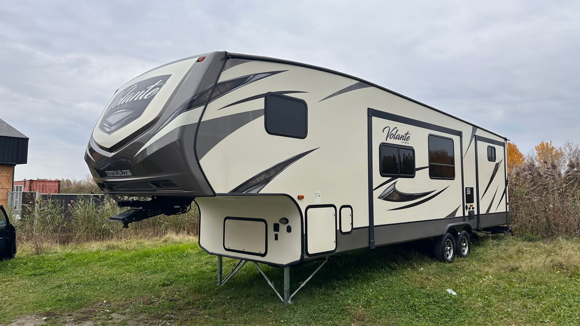 Caravane à sellette beige et grise garée sur l'herbe, sous un ciel nuageux.